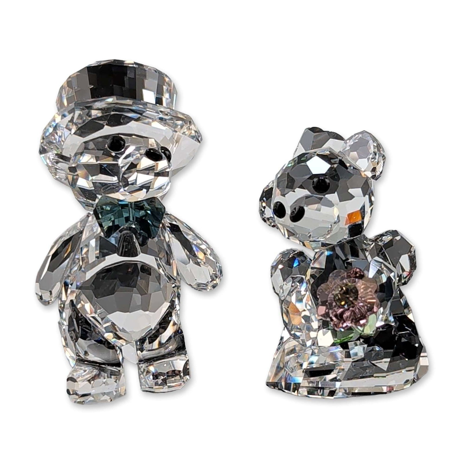 Swarovski Crystal Kris Bear Bride and Groom Figurines: Two Kris Bear figurines in faceted lead crystal, one depicted holding a pink crystal flower with green leaves, and the other wearing a crystal top hat and blue-teal bow tie. Both examples feature