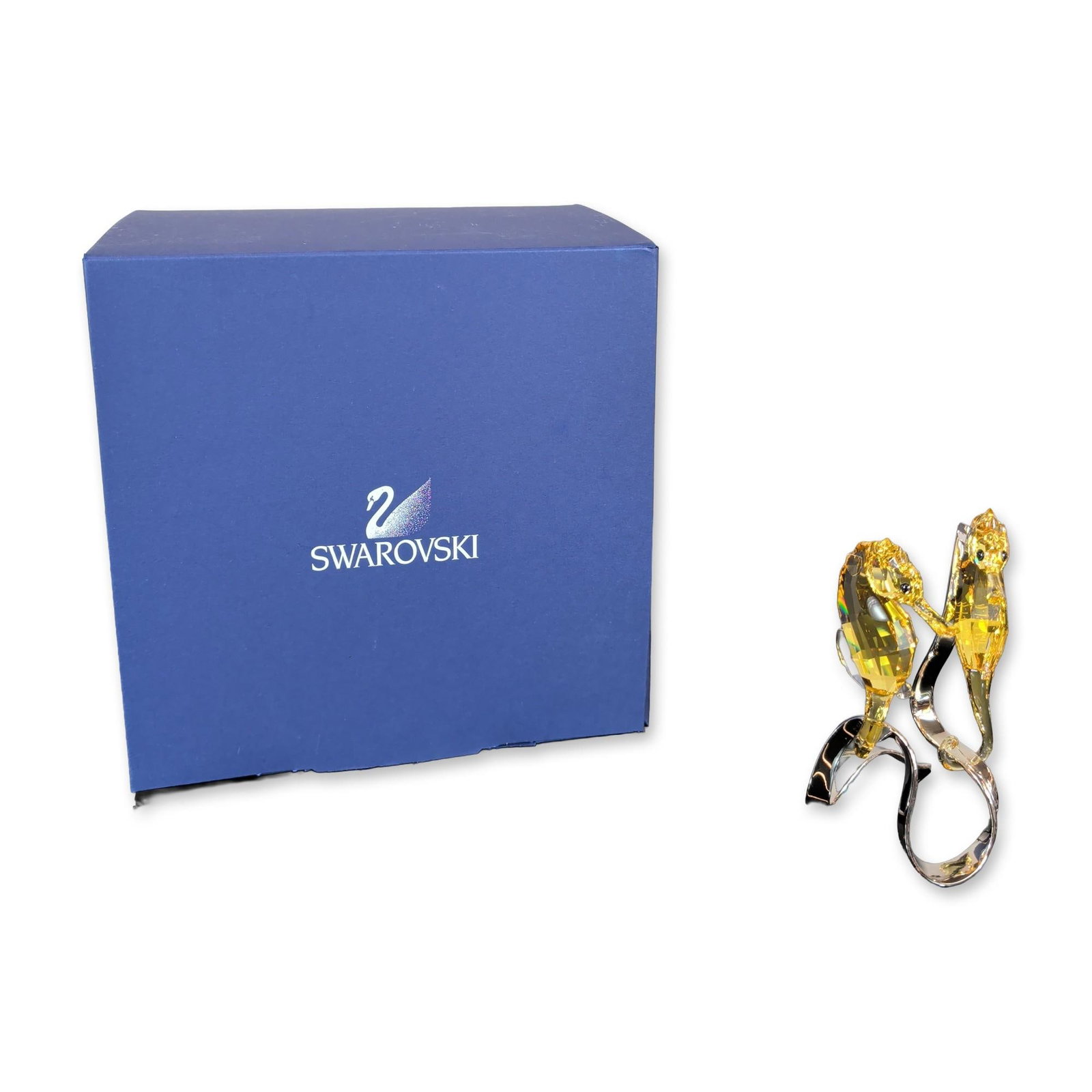 Swarovski Seahorses Light Topaz Figurine: The piece features two faceted Light Topaz amber-toned crystal seahorses with Jet black crystal eyes, mounted on a wave-form stand of polished silver-toned metal. The silver-toned metal base is etched