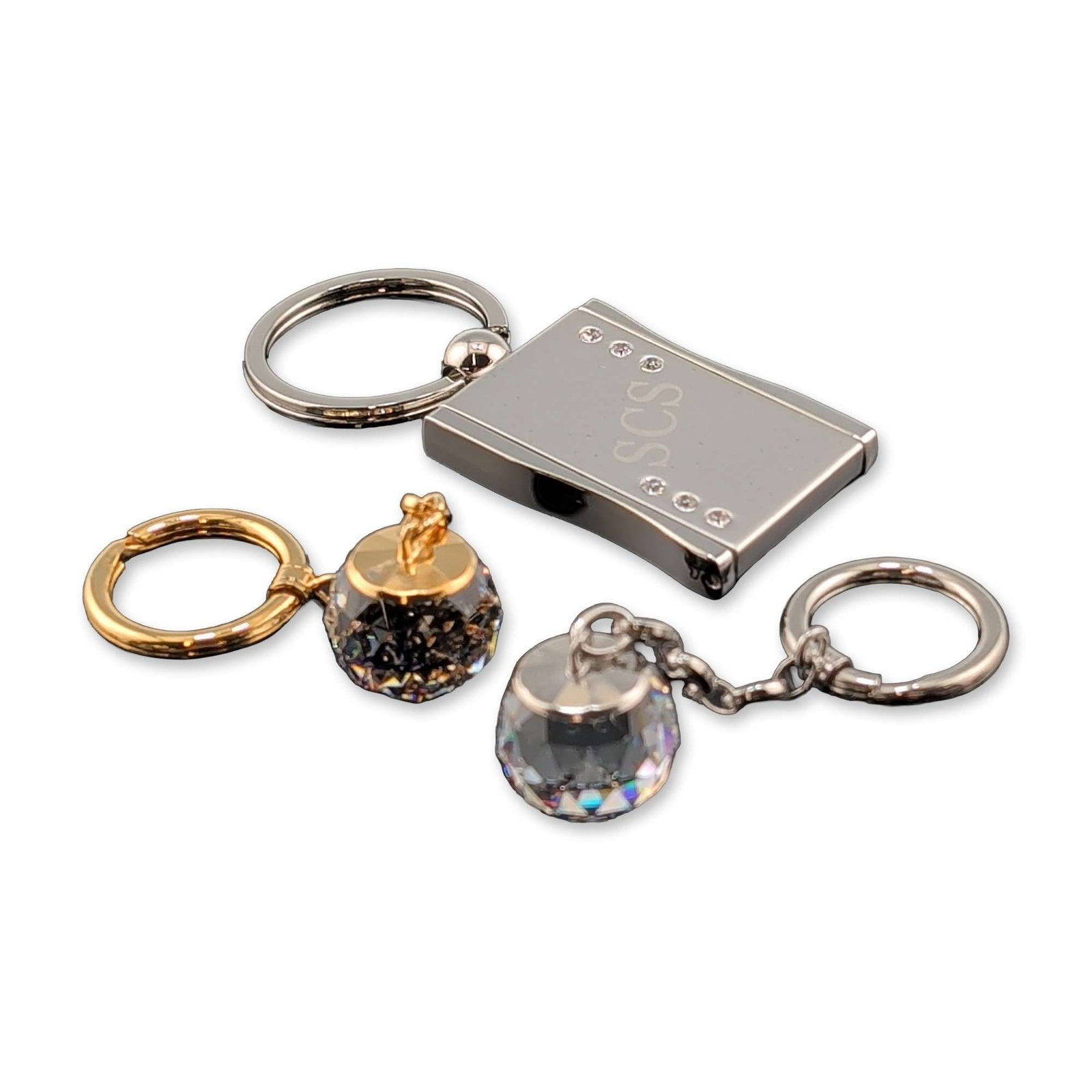 Collection of Three Swarovski Crystal Keychains: An assortment of three Swarovski decorative keychains. The collection includes a silver-tone rectangular locket-style photo frame charm engraved with SCS and accented with clear crystals. Also include