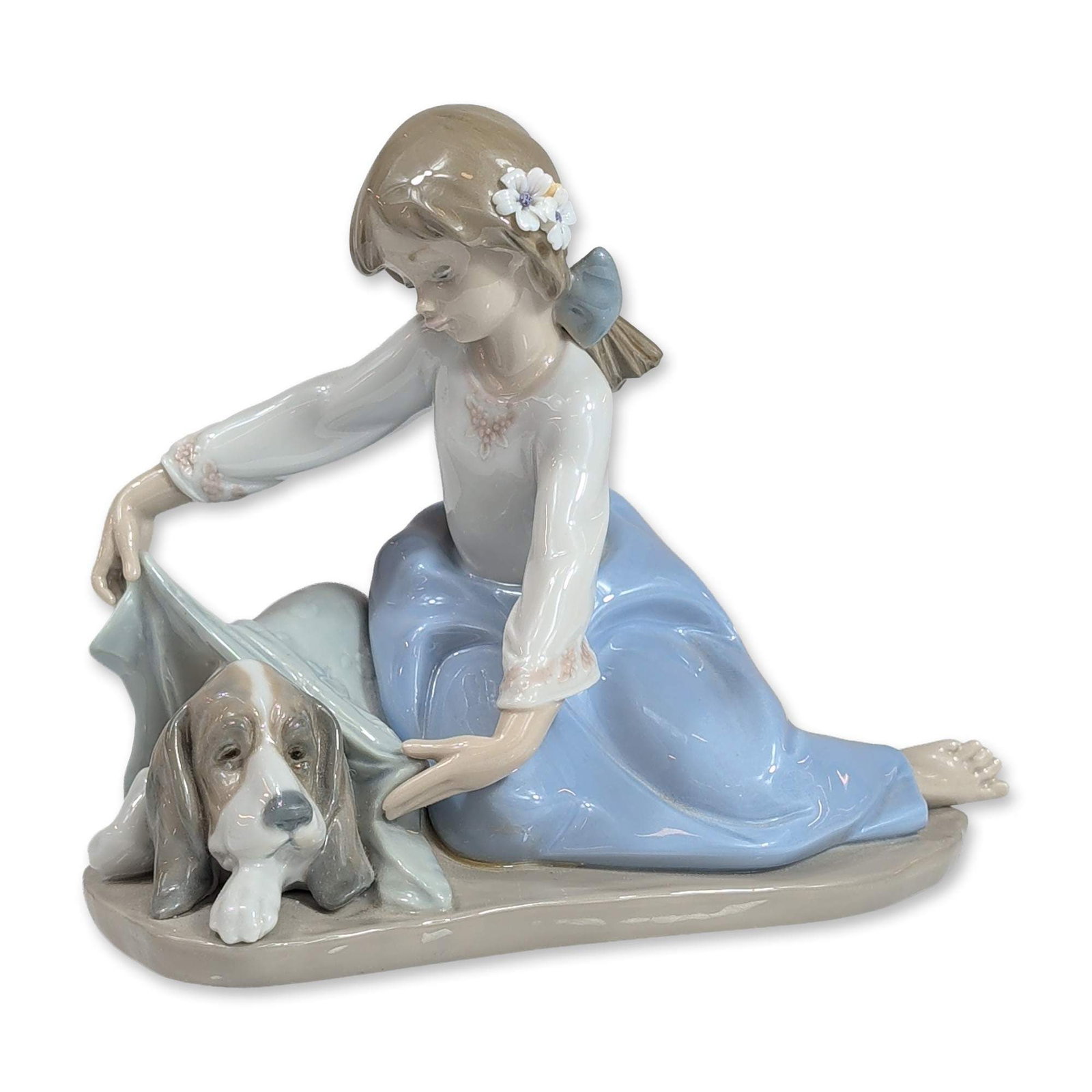 Lladro Spain Glazed Porcelain Dogs Best Friend Figurine 5688: Lladro, Spain. Glazed porcelain figurine titled Dogs Best Friend, model number 5688. The composition depicts a young girl in a white blouse and blue skirt kneeling to lift a pale blue cloth, revealing