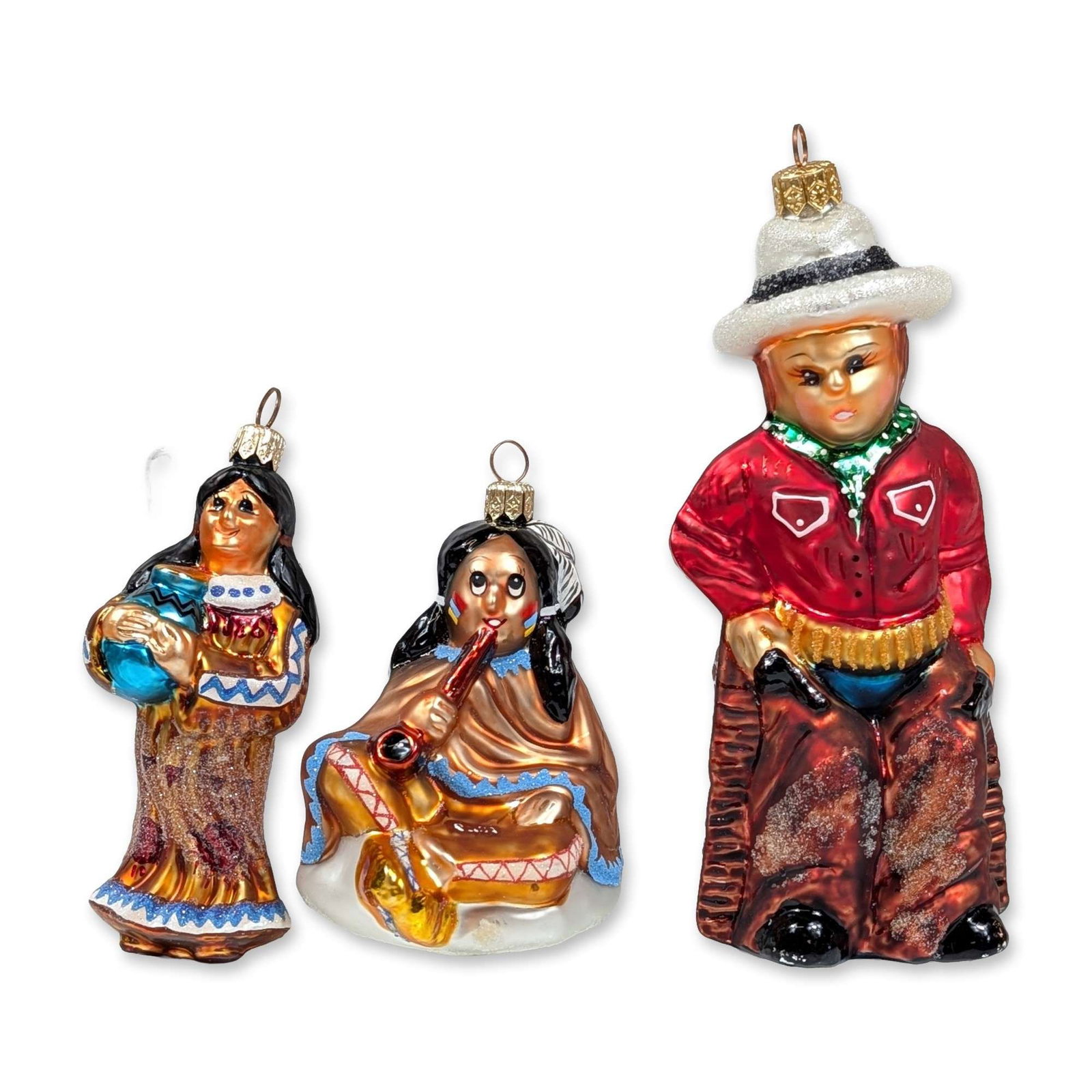 Three Christopher Radko Southwestern Glass Ornaments: Trio of mouth-blown and hand-painted glass figures featuring a standing indigenous female figure holding a blue olla, a seated flute player wrapped in a copper-toned blanket with blue trim, and The Du