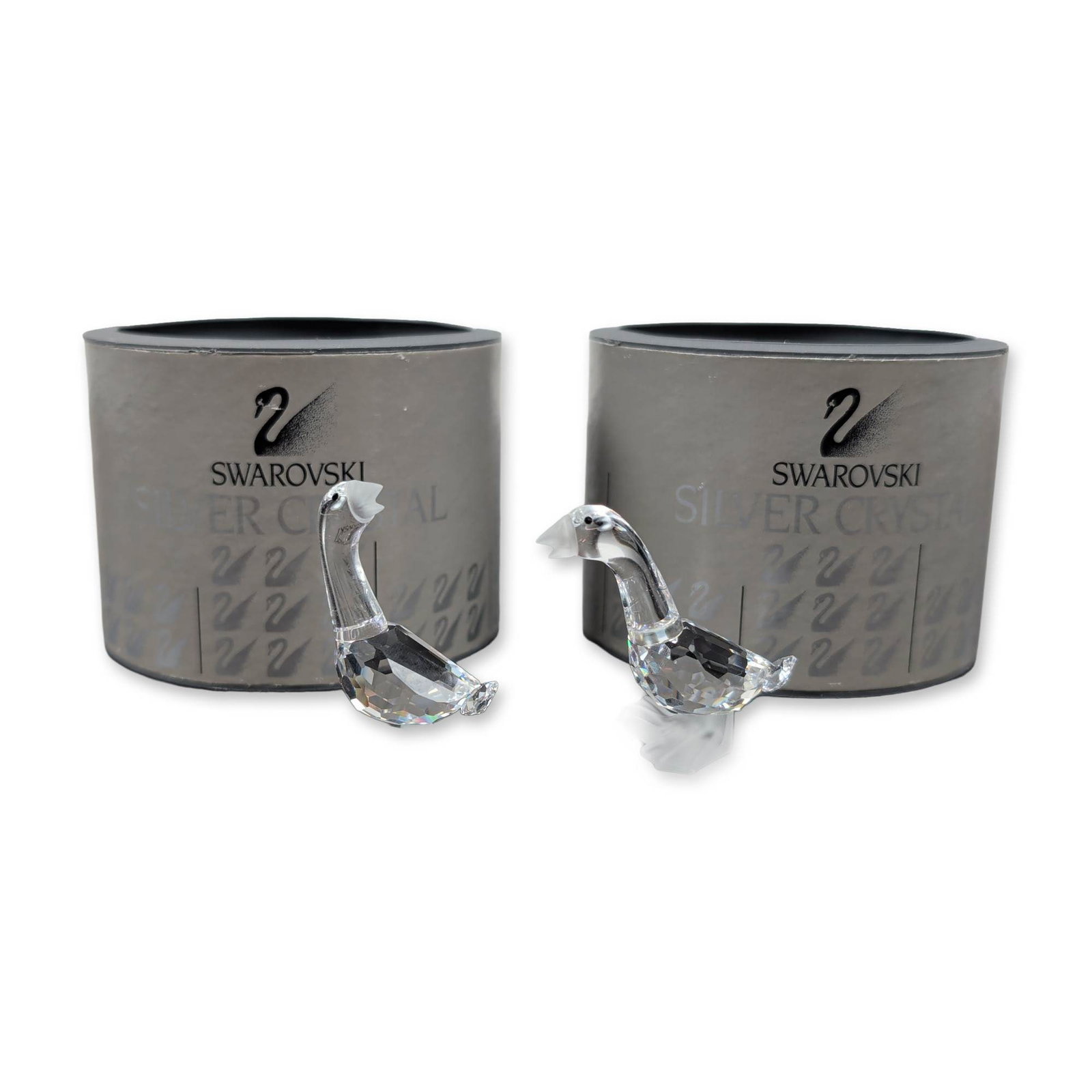 Swarovski Silver Crystal Pair of Gosling Figurines: Crafted in faceted clear lead crystal, this set of two features frosted crystal beaks and webbed feet. It includes one figurine with a raised head and another with a level head. Each bears the acid-et