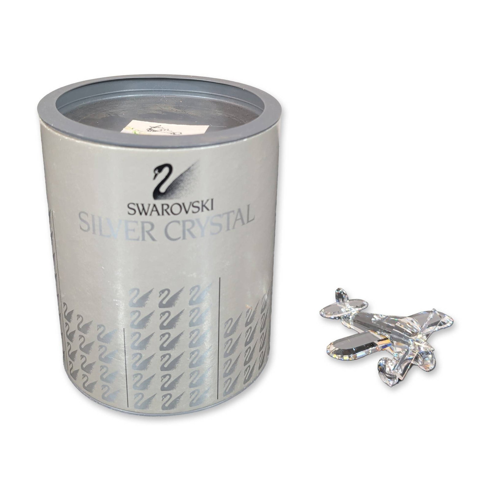 Swarovski Silver Crystal Airplane Figurine: Swarovski Silver Crystal biplane figurine in faceted clear crystal, designed by Adi Stocker. The stylized airplane features a multi-faceted fuselage, wings, and propeller. The underside of one tail wi