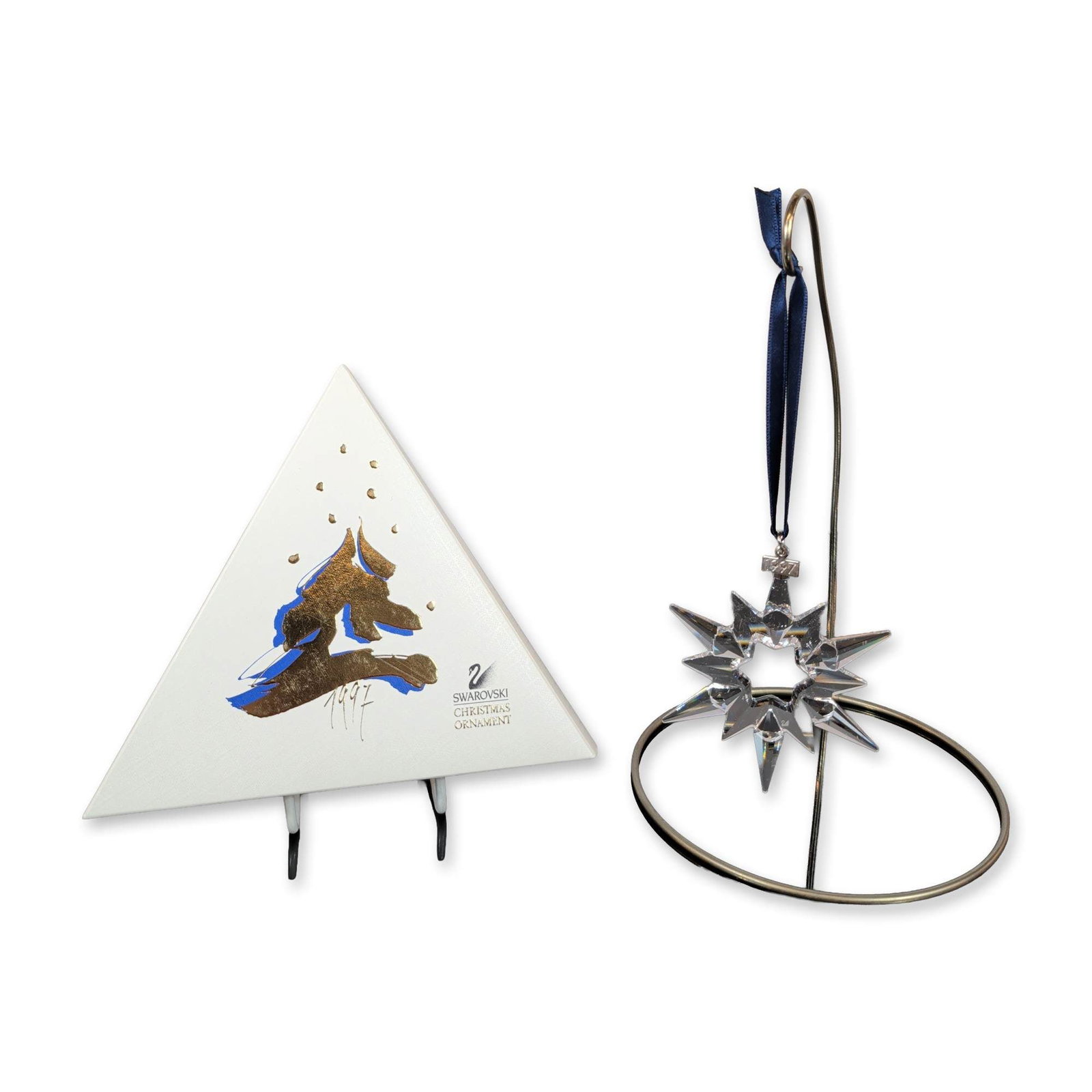 Swarovski 1997 Annual Edition Crystal Christmas Ornament: Swarovski (Austrian). 1997 Annual Edition Christmas ornament in faceted clear lead crystal, designed as a multi-pointed star with a central hexagonal aperture. The piece is suspended from a navy blue 