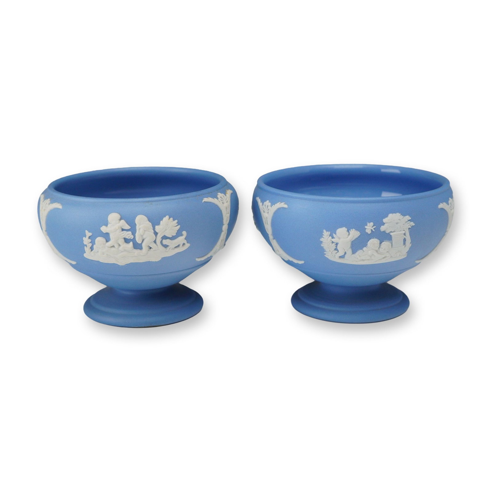 2pc Wedgwood Blue Dipped Jasperware Footed Mini Bowls: A pair of Wedgwood Jasperware footed mini bowls featuring a matte light blue exterior and glazed blue interior. These circular bowls are embellished with white bas-relief sprigging in Neoclassical pat