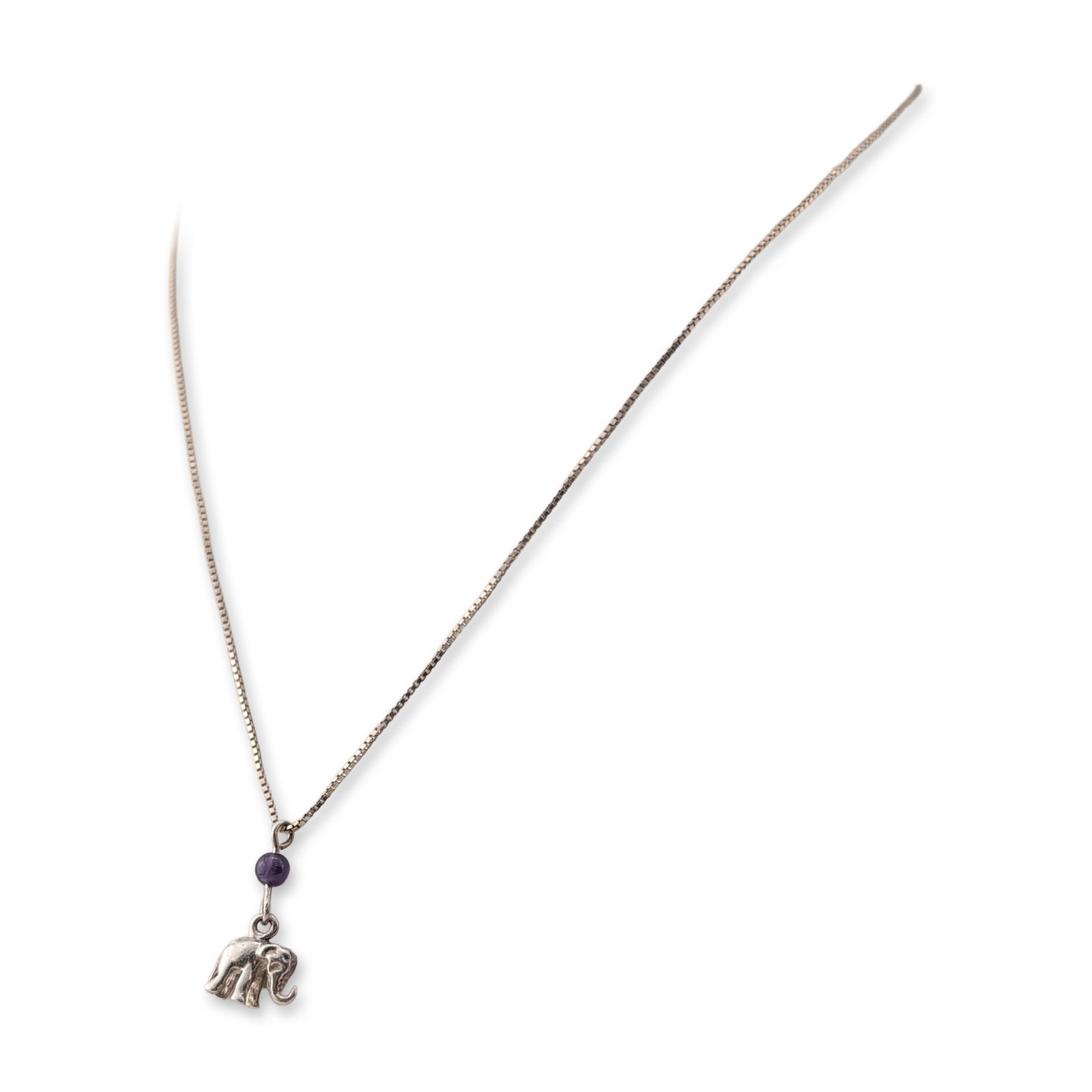 Sterling Silver Elephant and Amethyst Pendant Necklace: Sterling silver necklace featuring a cast elephant pendant with a raised trunk. The pendant is accented with a single spherical amethyst bead positioned directly above the elephant charm. The piece in