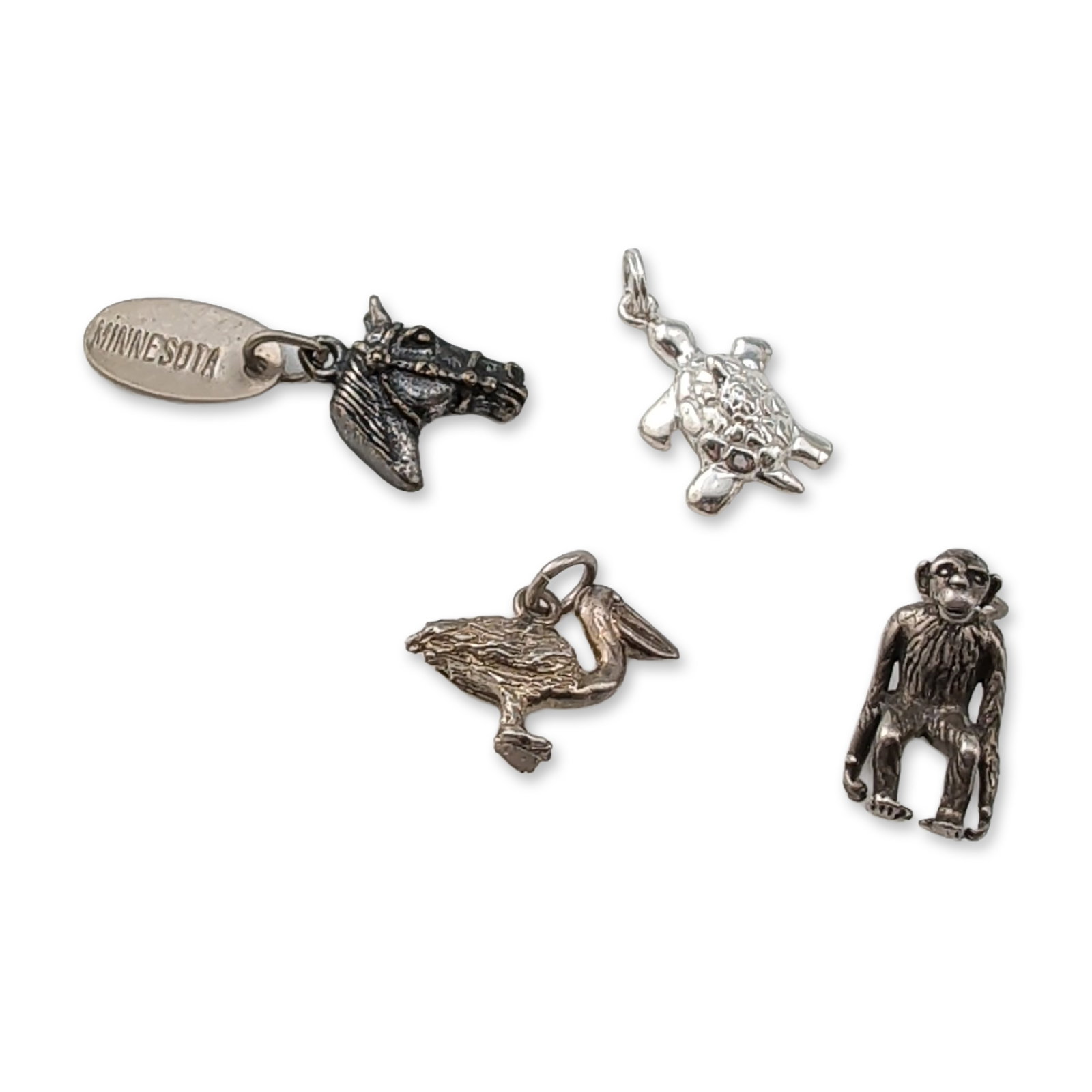 4pc Collection of Sterling Silver Animal Charms: An assortment of animal-themed charms in sterling silver, featuring a primate, a turtle, a pelican, and a horse head. The turtle charm is stamped 925 on the reverse with additional indistinct