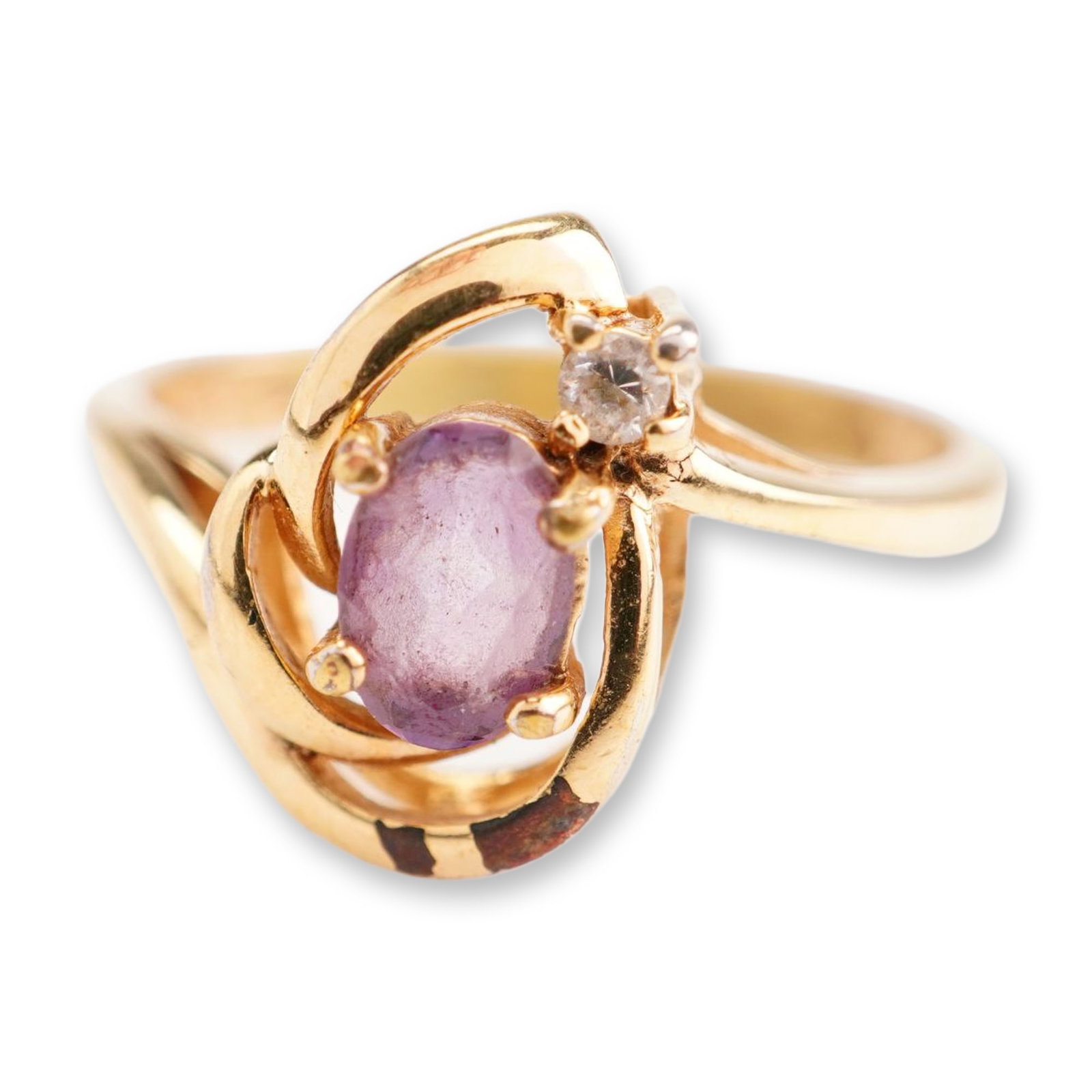 Gold Plated Fashion Ring with Oval Purple Stone: This gold-plated fashion ring features a bypass-style head with decorative swirling ribbon elements. The setting contains one prong-set oval-cut translucent purple stone and one small round-cut clear 