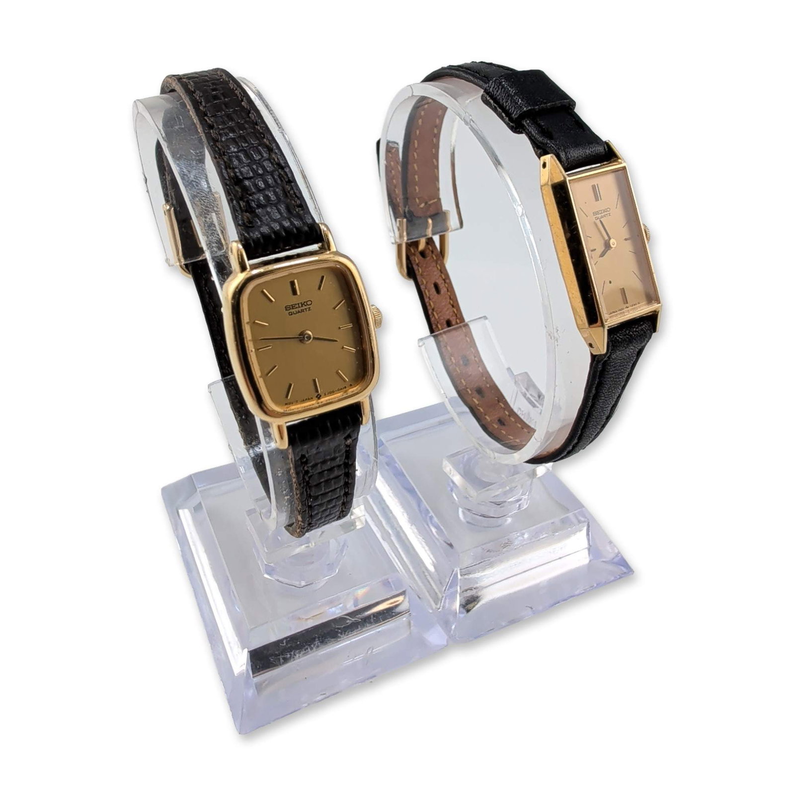 Two Vintage Seiko Gold-Tone Wristwatches: Seiko. Pair of vintage ladies' quartz wristwatches featuring gold-tone cases and black leather straps. One timepiece has a rectangular case with a brushed gold-tone dial and baton indices; case back