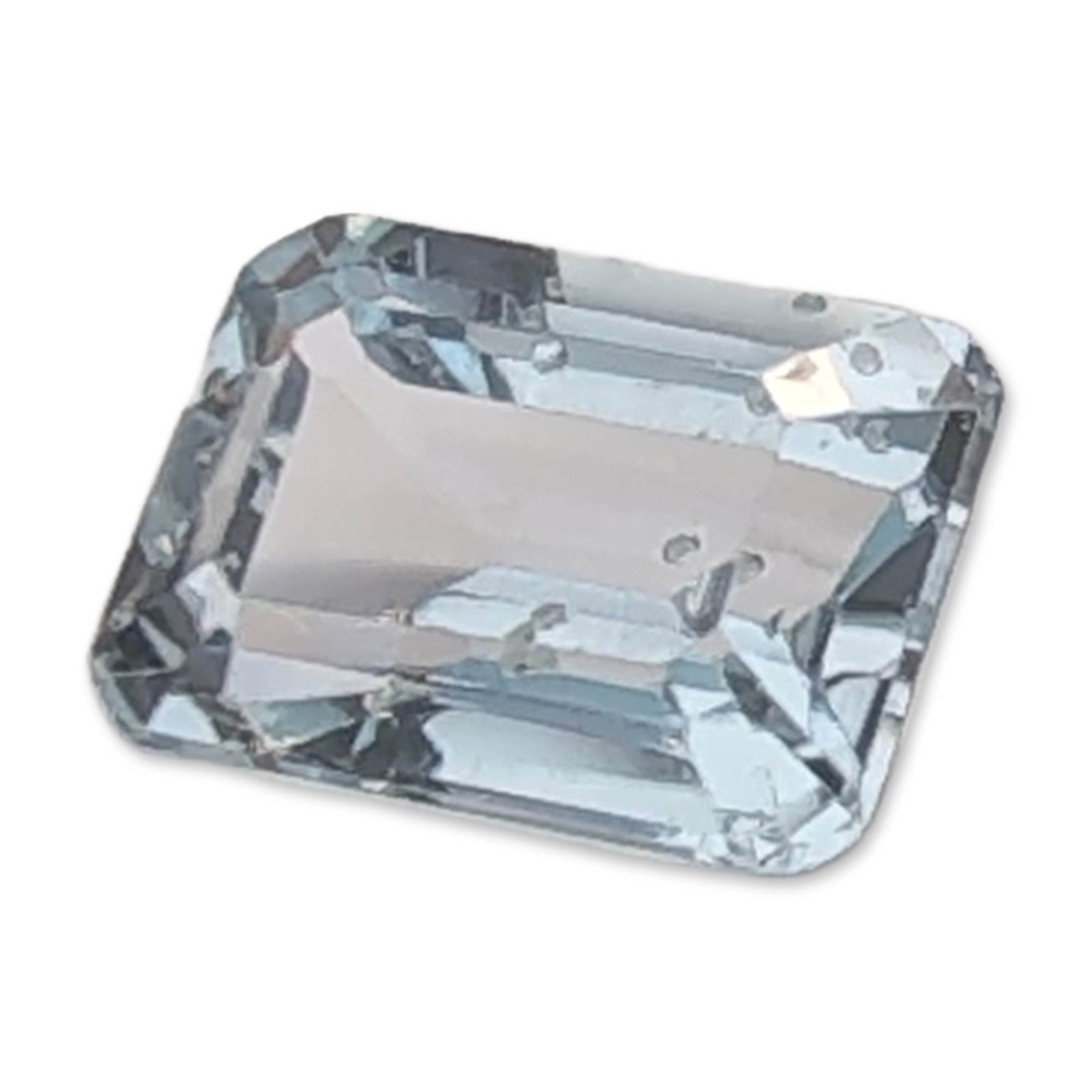 Emerald Cut Topaz Gemstone: Loose Topaz gemstone featuring a rectangular emerald cut with truncated corners. The stone exhibits a transparent, very pale blue color with visible internal needle-like inclusions, often referred to 