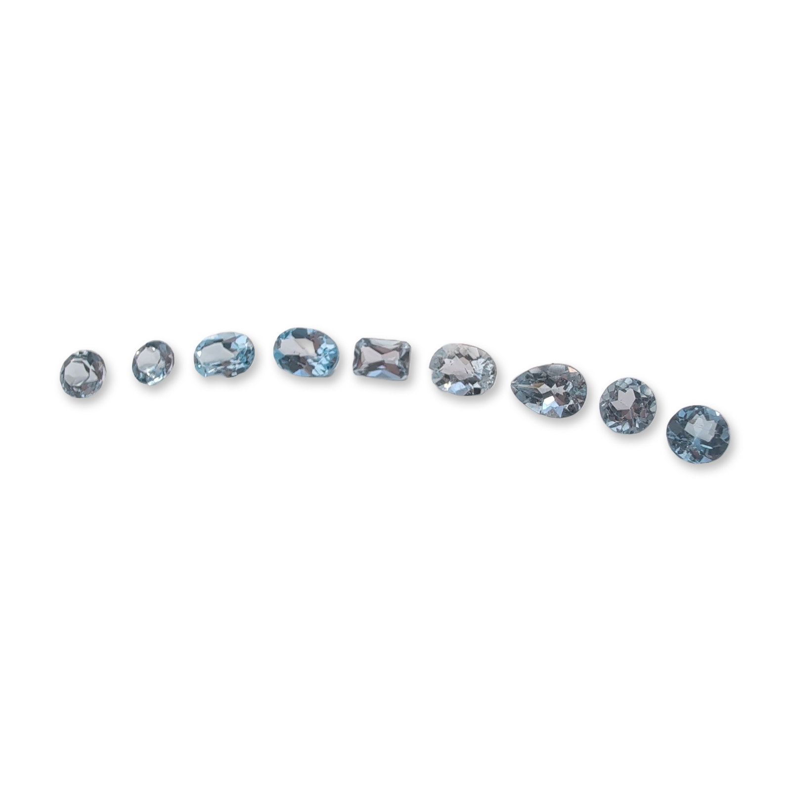 Group of Nine Loose Faceted Blue Gemstones: Group of nine loose faceted gemstones featuring a pale to light blue color. The set includes four round brilliant cuts, three oval cuts, one pear cut, and one rectangular emerald cut. The stones appea