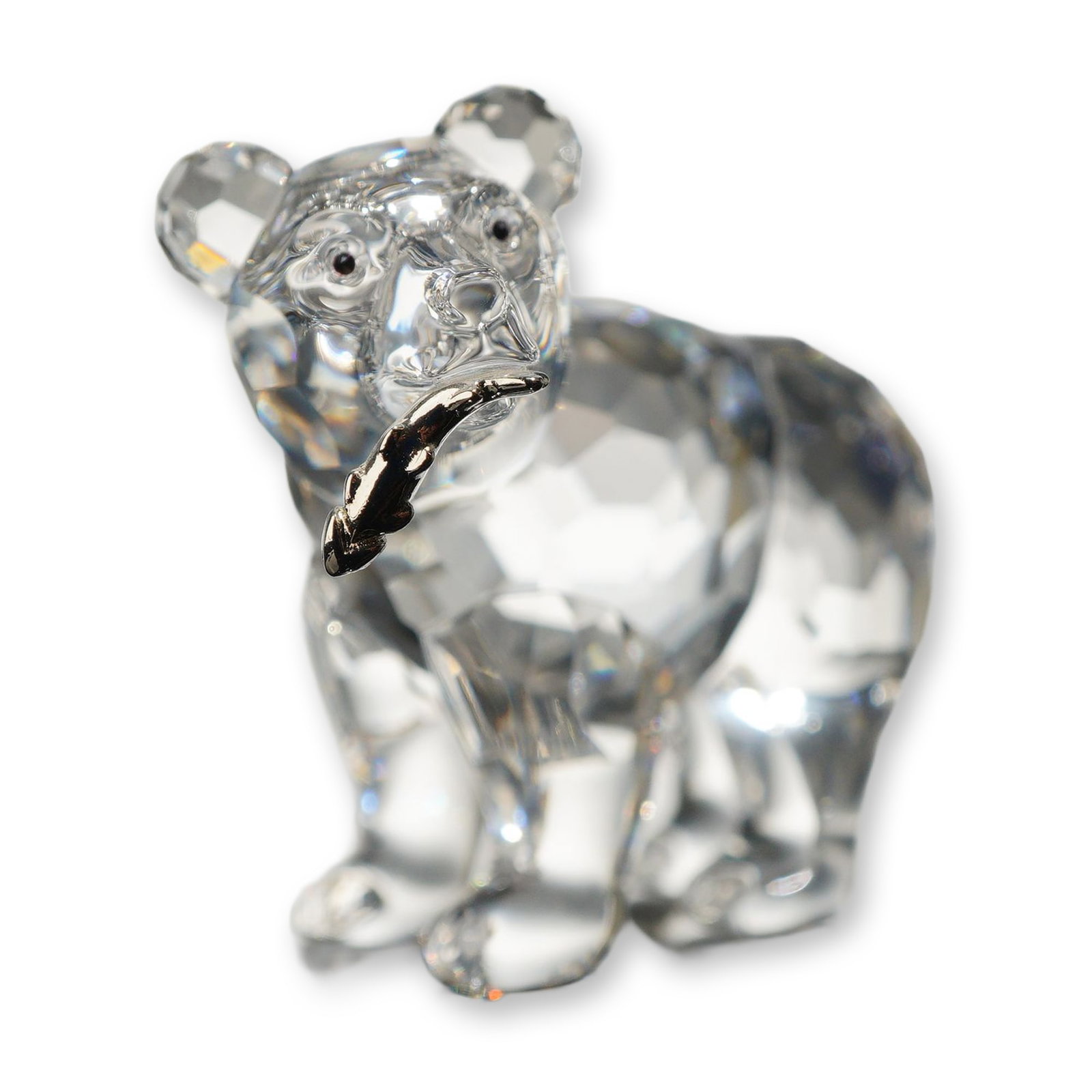 Swarovski Crystal Grizzly Cub with Fish Figurine: Swarovski. Figurine of a grizzly bear cub in faceted clear crystal, depicted standing and holding a silver-toned metal fish in its mouth. Features black crystal eyes. Marked with the laser-etched Swar