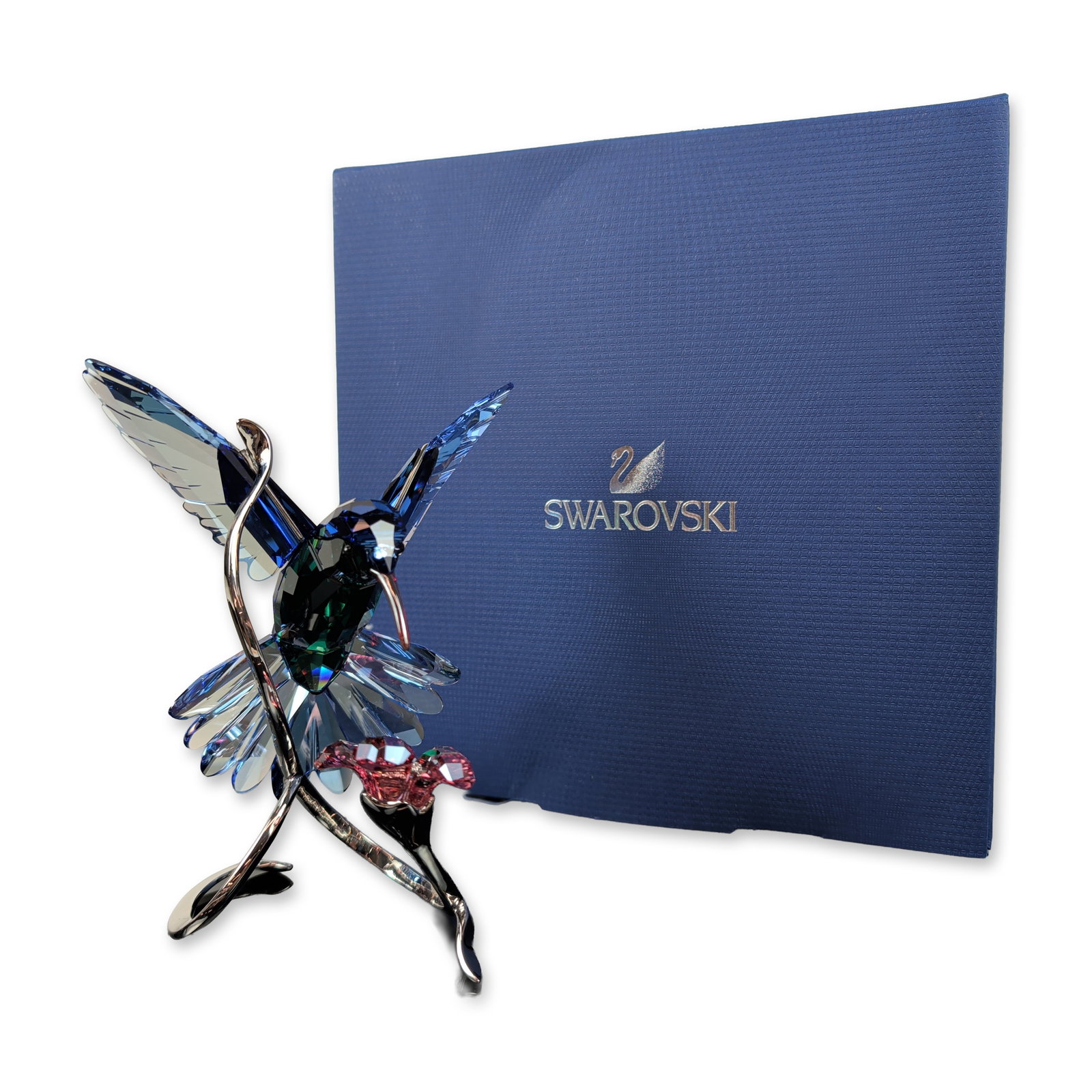 Swarovski Crystal Paradise Birds Figurine, Hummingbird: A stunning Swarovski Hummingbird figurine crafted from multi-tonal faceted crystal, showcasing deep blue wings and tail feathers, a vivid emerald-green body, and a delicate pinkish-red beak. The bird 