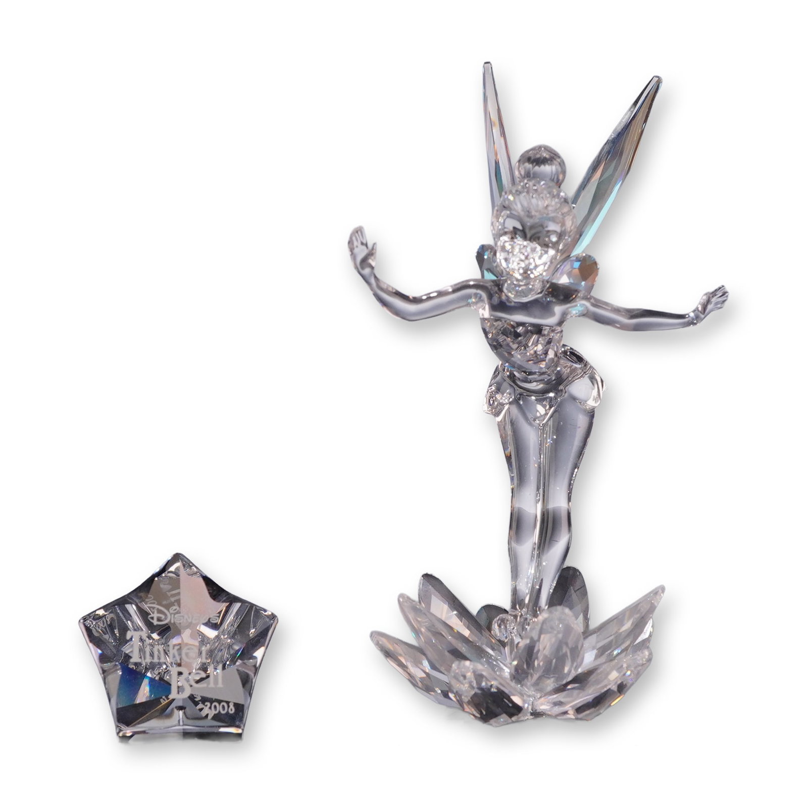 Swarovski Crystal Tinker Bell Figurine and Plaque Set: Swarovski crystal Tinker Bell figurine, released in 2008, accompanied by its coordinating star-shaped title plaque. The faceted lead crystal figure depicts the Disney character Tinker Bell standing on