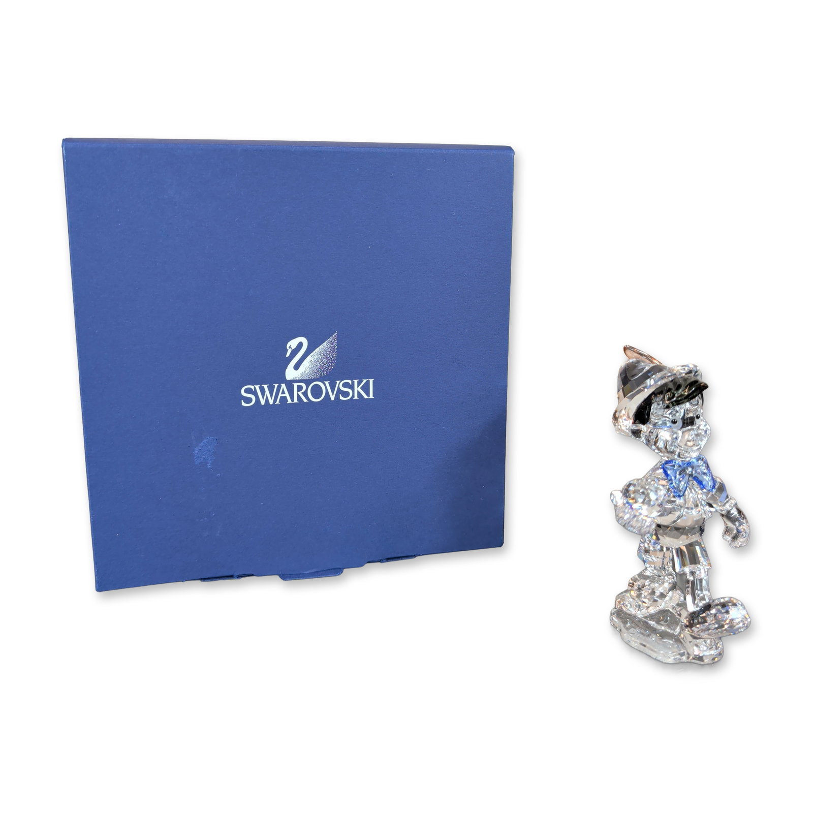 Swarovski Disney Crystal Figurine, Pinocchio: Figurine of Disney's Pinocchio in faceted clear crystal, featuring color accents including a blue crystal bow tie, black hat, and an orange and red crystal feather. Pinocchio is depicted in a dynamic 