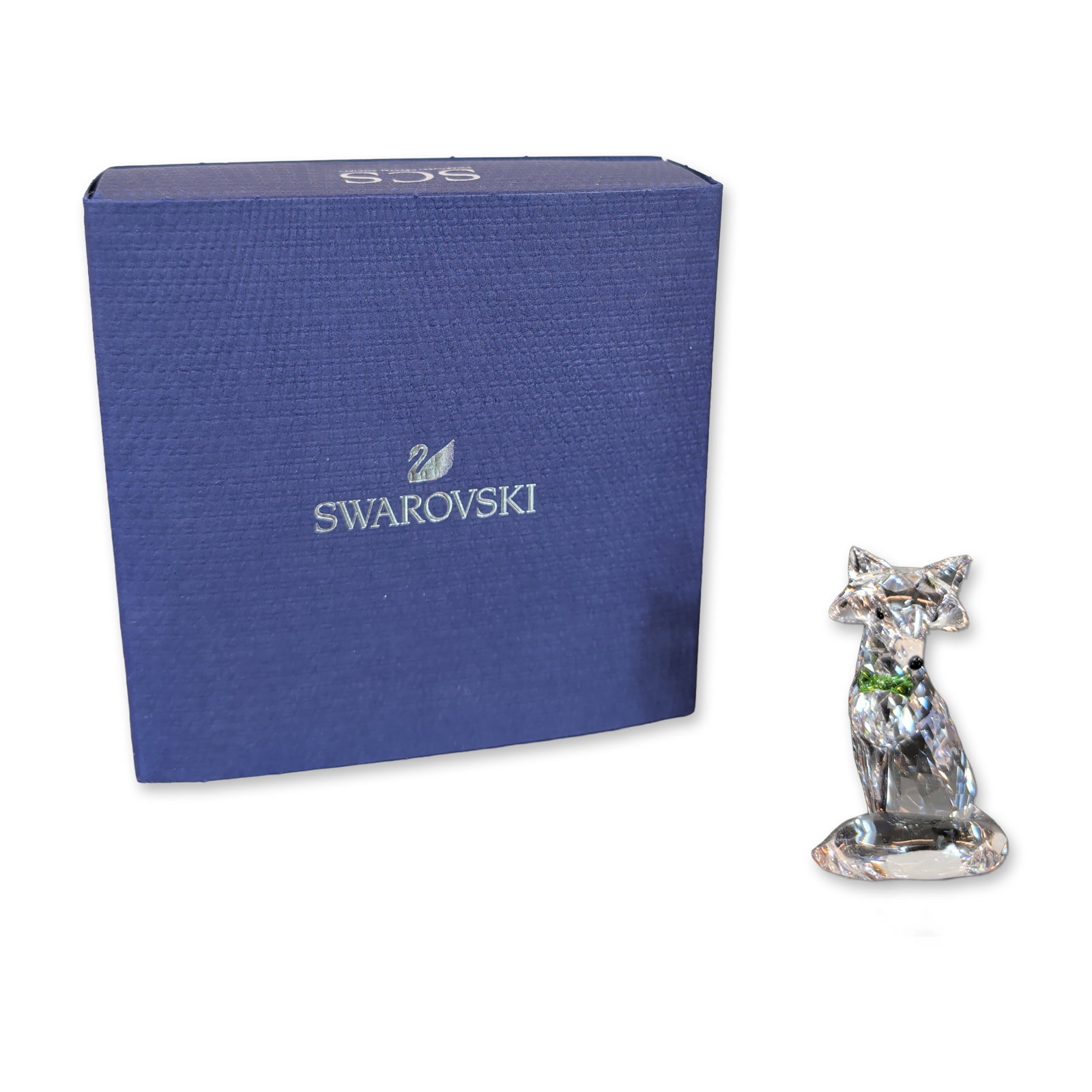 Swarovski SCS Faceted Crystal Artic Fox Figurine: Swarovski Crystal Society (SCS) figurine depicting an Artic Fox, crafted in clear faceted crystal. The piece features pointed ears, small black crystal eyes, and a vibrant green crystal bow-tie. The f