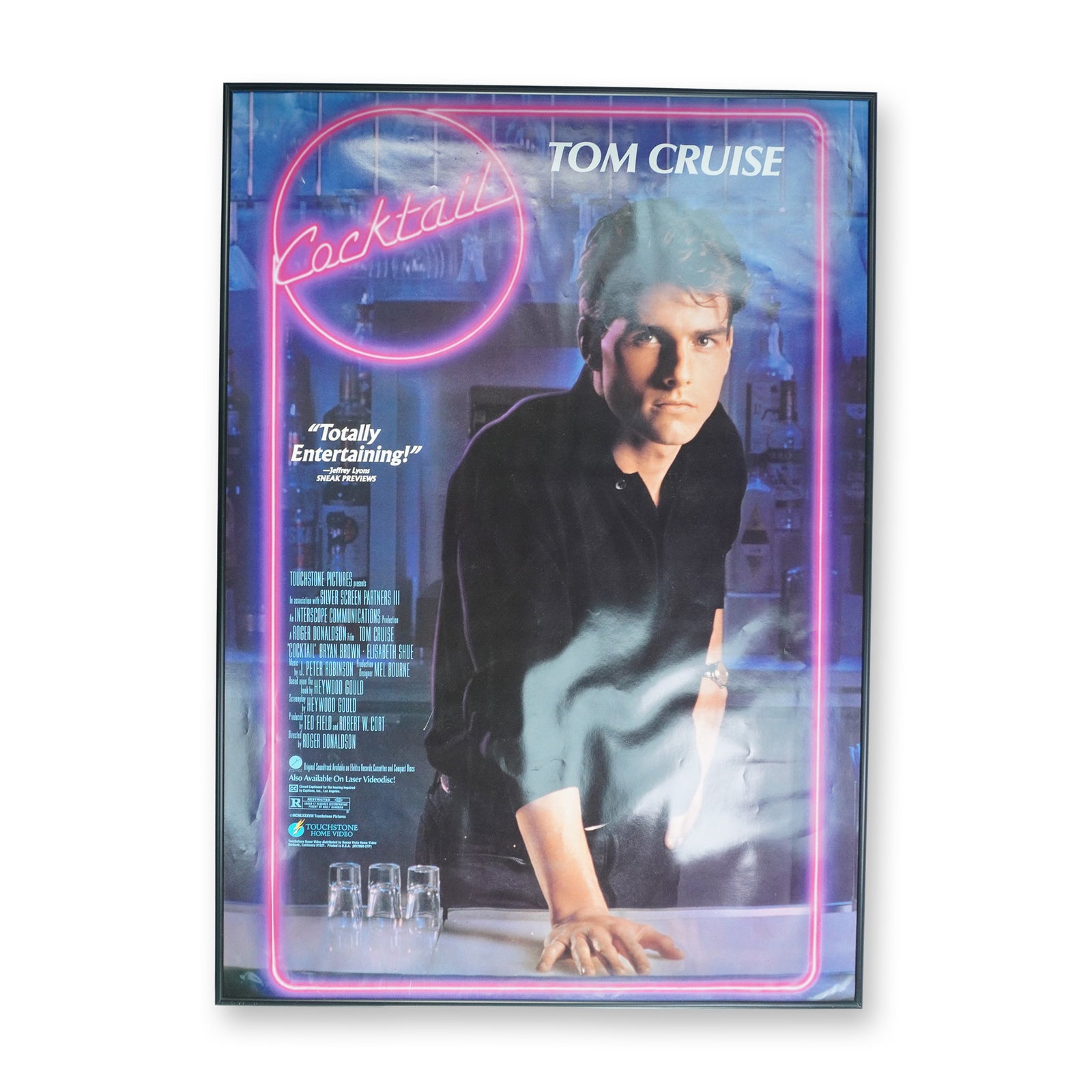 Touchstone Pictures Framed Movie Poster, Cocktail: A framed movie poster for the 1988 Touchstone Pictures film 'Cocktail'. The movie stars Tom Cruise, Bryan Brown, and Elisabeth Shue and is directed by Roger Donaldson. The poster is housed in a black 