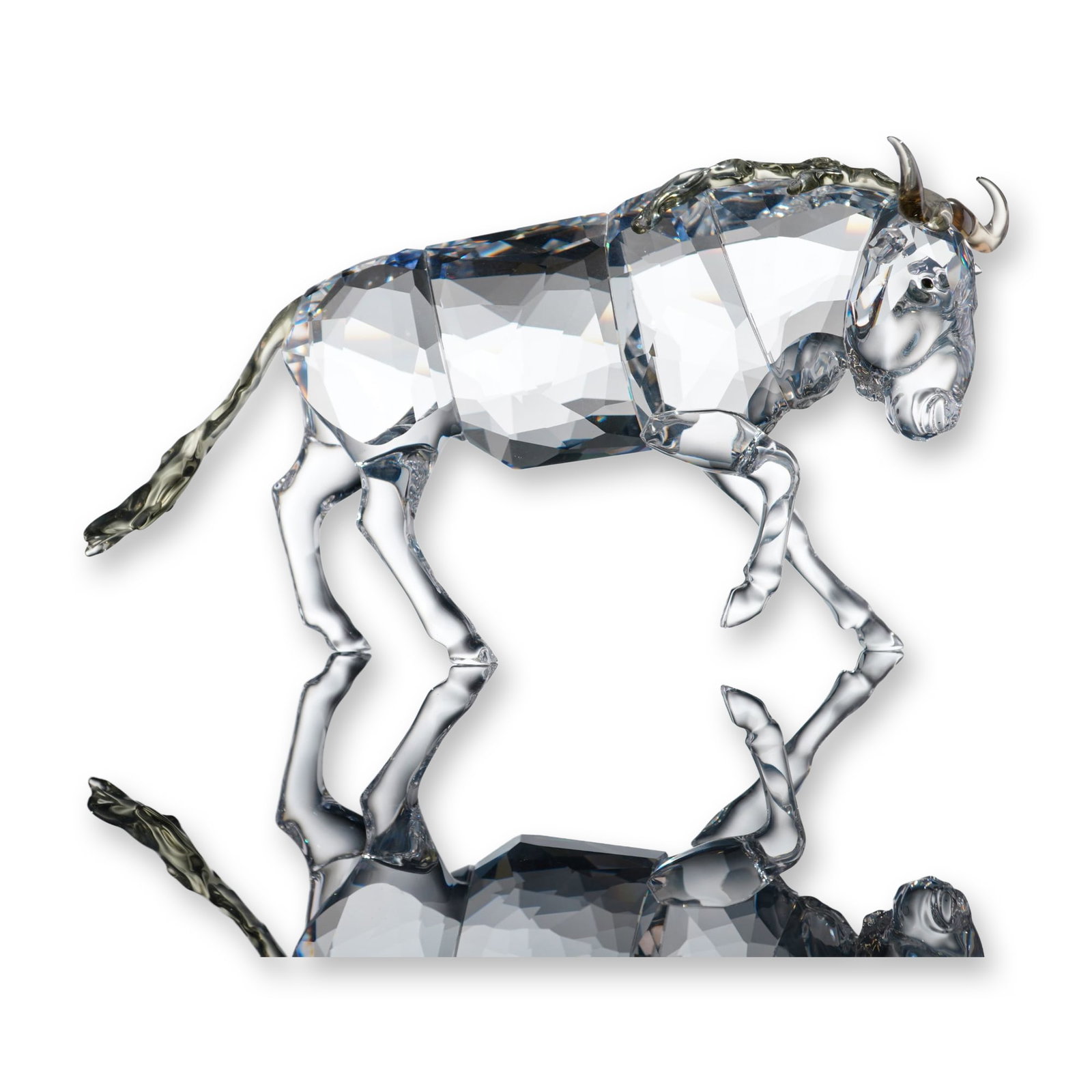 Swarovski Crystal Figurine, Gnu: Swarovski crystal figurine depicting a gnu, also known as a wildebeest, in a walking pose with one foreleg raised. The piece is constructed from faceted clear lead crystal with contrasting smoky-grey 