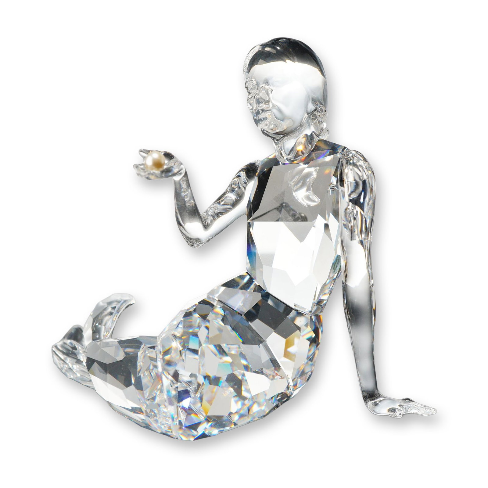 Swarovski Crystal Mermaid Figurine: Swarovski clear crystal mermaid figurine, depicted in a seated pose leaning on her left arm, holding a cream-colored faux pearl in her raised right hand. The figure features a smooth, satin-finished u