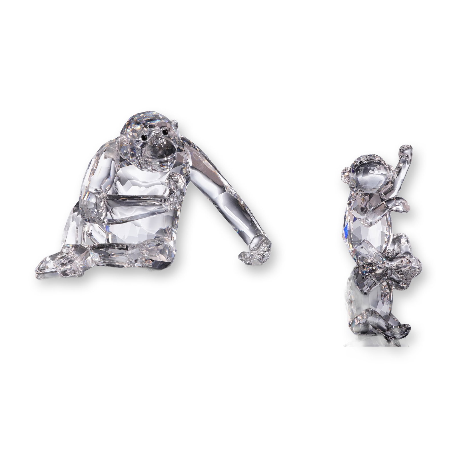 Swarovski Crystal Chimpanzee and Chimp Figurines: The set includes a seated mother figure leaning on her left arm with black crystal eyes, and a smaller seated baby figure with a raised left arm. Both pieces feature multi-faceted polished bodies. Mar