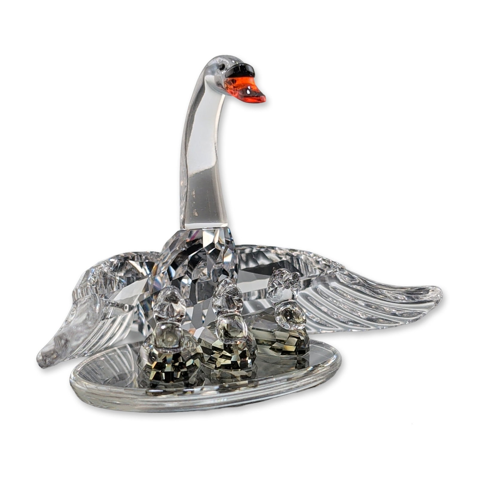 Swarovski Silver Crystal Swan Family Figurine: Swan Family figurine in faceted lead crystal, part of the Beauties of the Lake series. The clear crystal mother swan features spread wings, a smooth neck, and an orange-red beak. Three smaller faceted