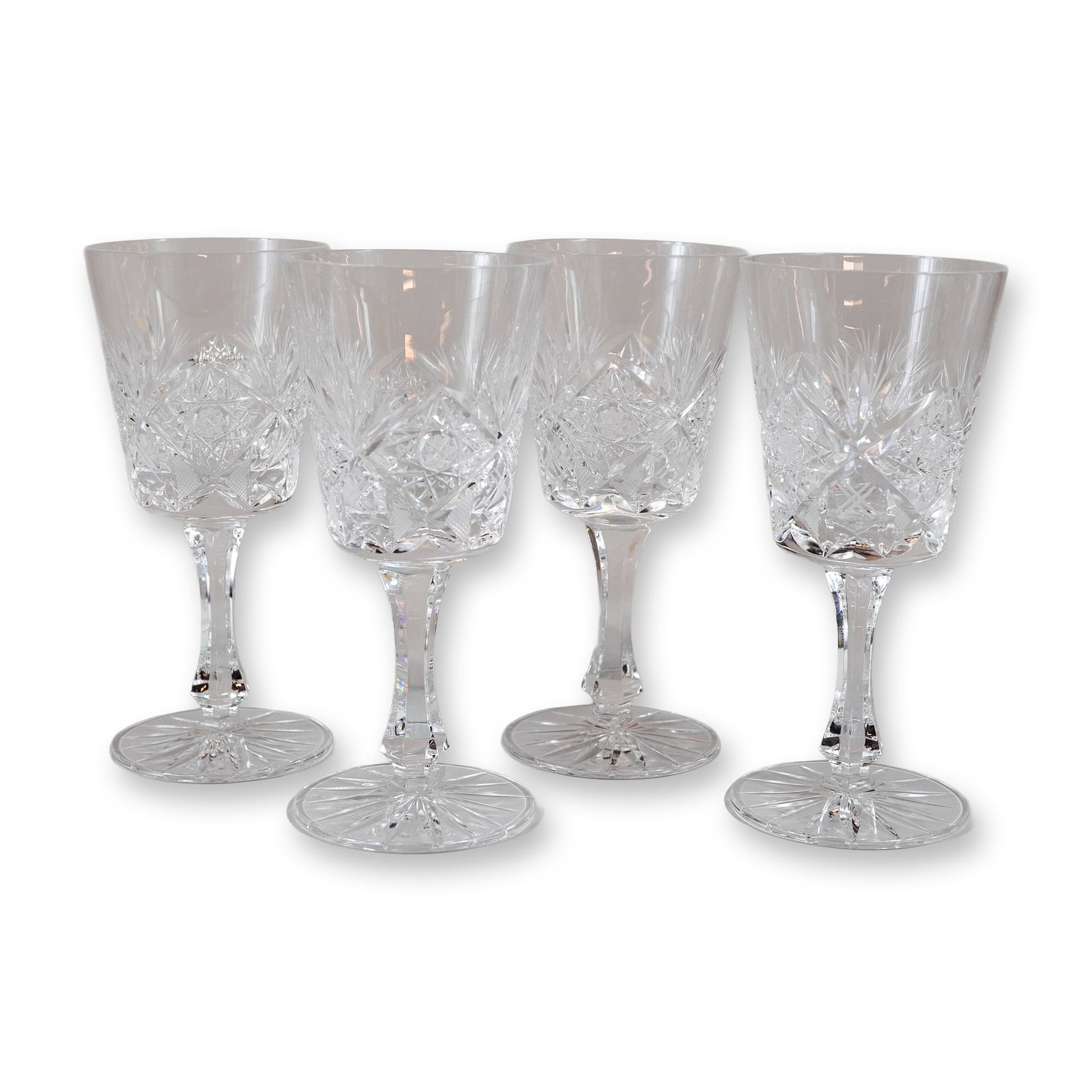 Set of Four Cut Crystal Stemware Glasses in the Star and Fan Pattern: This set of four crystal glasses features a deep, slightly tapered cylindrical bowl decorated with a complex geometric pattern. The design includes a central band of large rosettes with crisscrossed