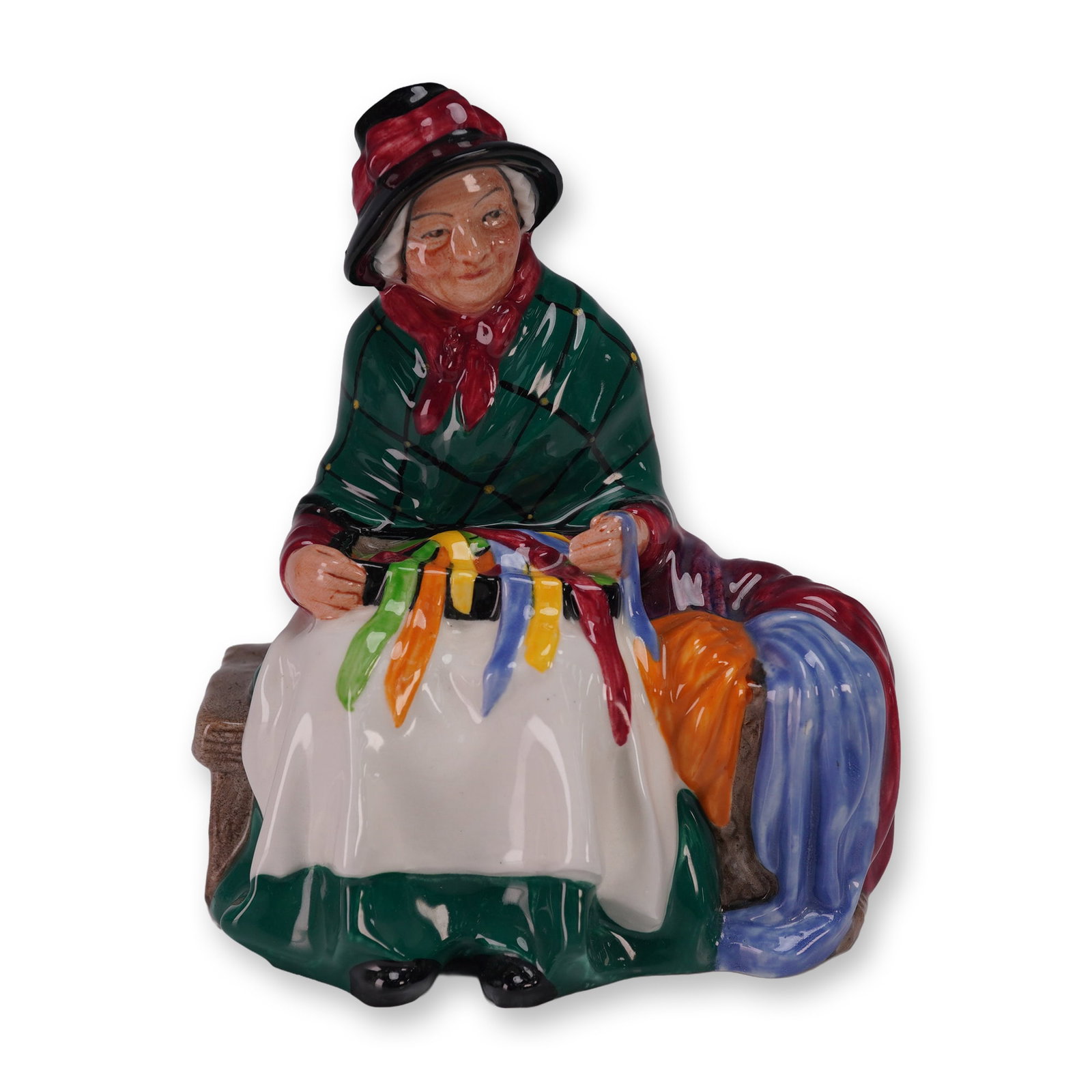 Royal Doulton Figurine, Silks and Ribbons HN2017: Royal Doulton hand painted porcelain figurine titled Silks and Ribbons HN2017, modeled as an elderly woman seated with brightly colored ribbons draped across her lap and shawls at her side, designed b