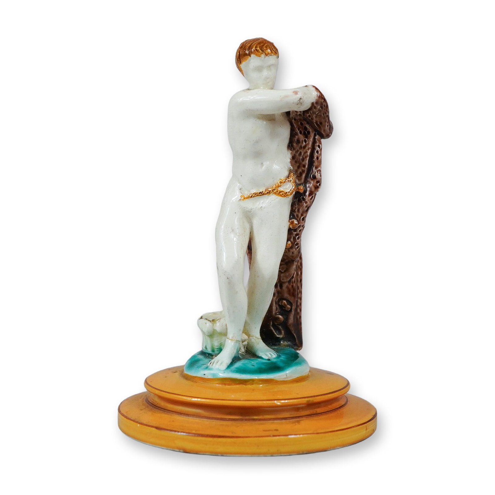 Porcelain Figurine of a Youth with Pelt: A glazed porcelain figurine depicting a standing youth, partially nude, holding a textured and spotted brown pelt over his left shoulder. The figure is accented with a delicate gilded chain at the wai