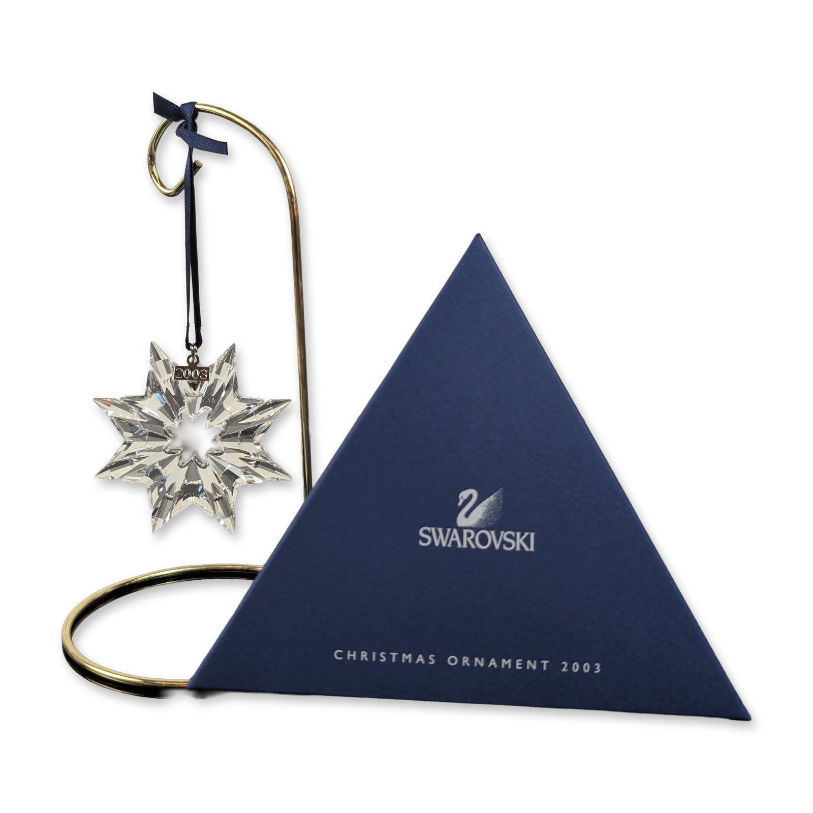 Swarovski 2003 Annual Edition Crystal Snowflake Ornament: Swarovski Christmas ornament in faceted lead crystal, featuring a multi-pointed snowflake design with a central star-shaped cutout. Suspended by a navy blue ribbon with a silver-toned metal bale stamp