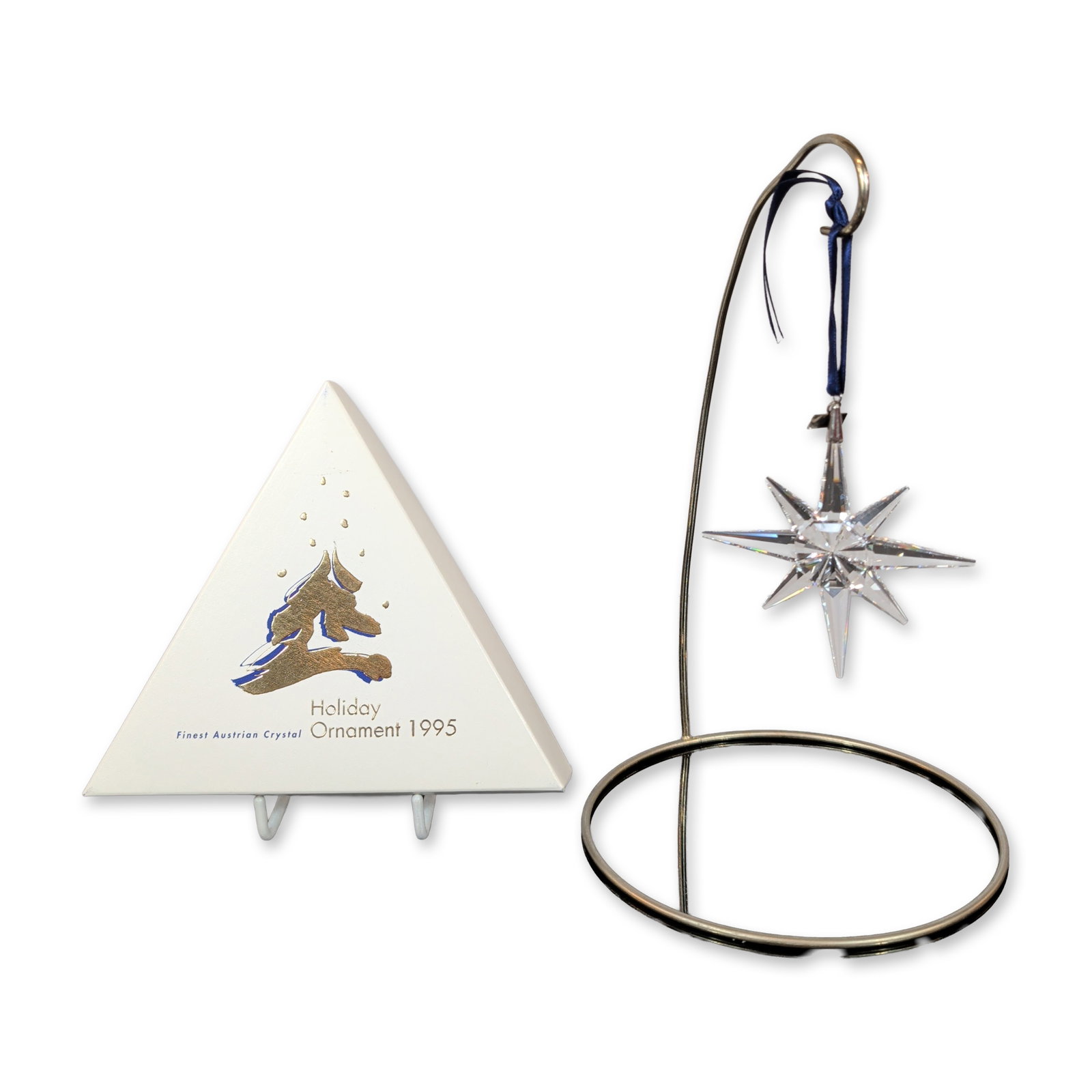 Swarovski 1995 Annual Edition Christmas Ornament: Swarovski 1995 Annual Edition Christmas ornament in faceted clear lead crystal, designed as a multi-pointed star. The piece is suspended from a blue satin ribbon featuring a gold-tone metal hang-tag s