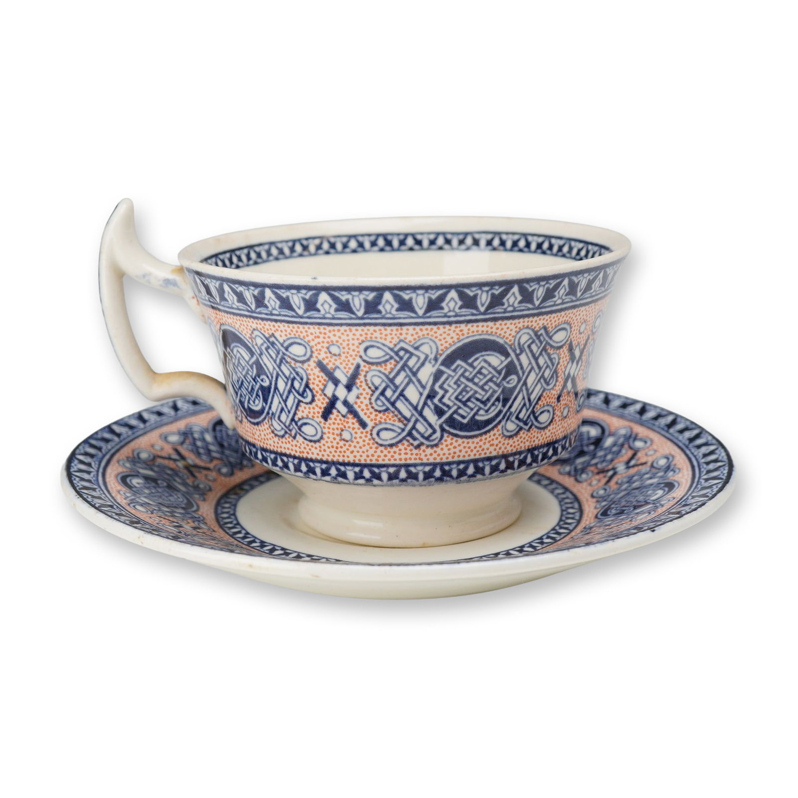 2pc Wedgwood Lindisfarne Pattern Teacup and Saucer: A teacup and matching saucer manufactured by Wedgwood in the Lindisfarne pattern. This Celtic Revival design is transfer-printed in cobalt blue against a salmon-orange stippled background. The pattern
