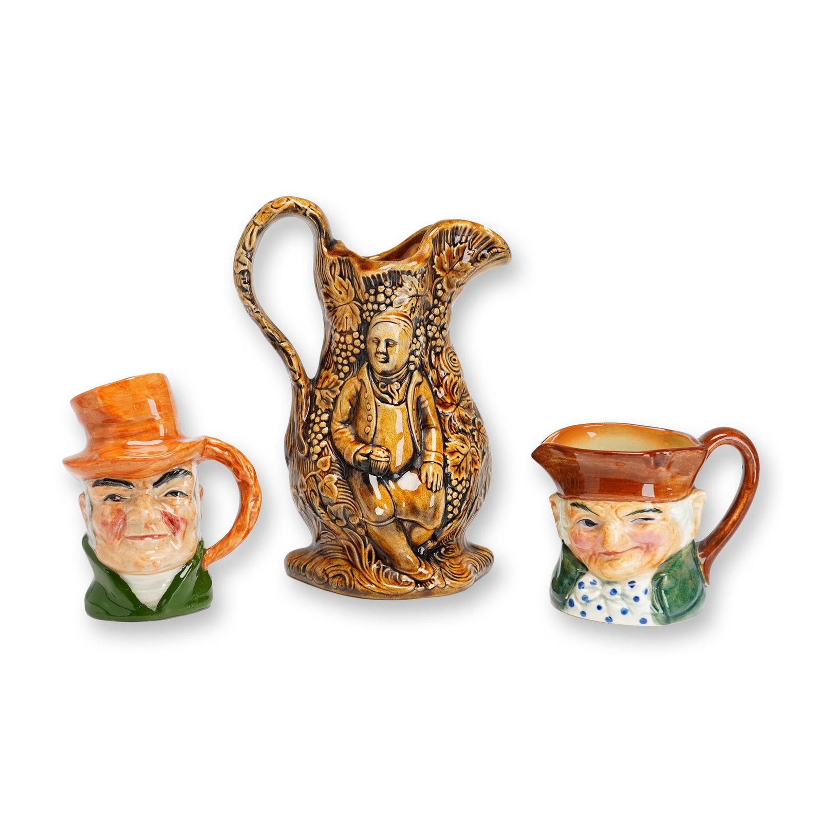 Three English and Japanese Porcelain Pottery Pitcher and Character Jugs: Lot includes brown relief pitcher with man, leaves and fruit plus two small character jugs, one marked Occupied Japan and the other with faint green mark. Largest piece is 7.75"H. Dimensions: 5.75"L x