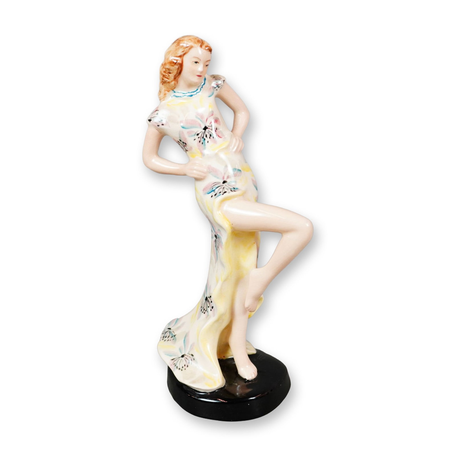 Goldscheider Art Deco Porcelain Dancer Figurine: Hand-painted figurine depicting a young woman in a flowing white dress accented with blue and yellow details and decorated with a pink and blue floral motif. Posed with her hands on her hips, she