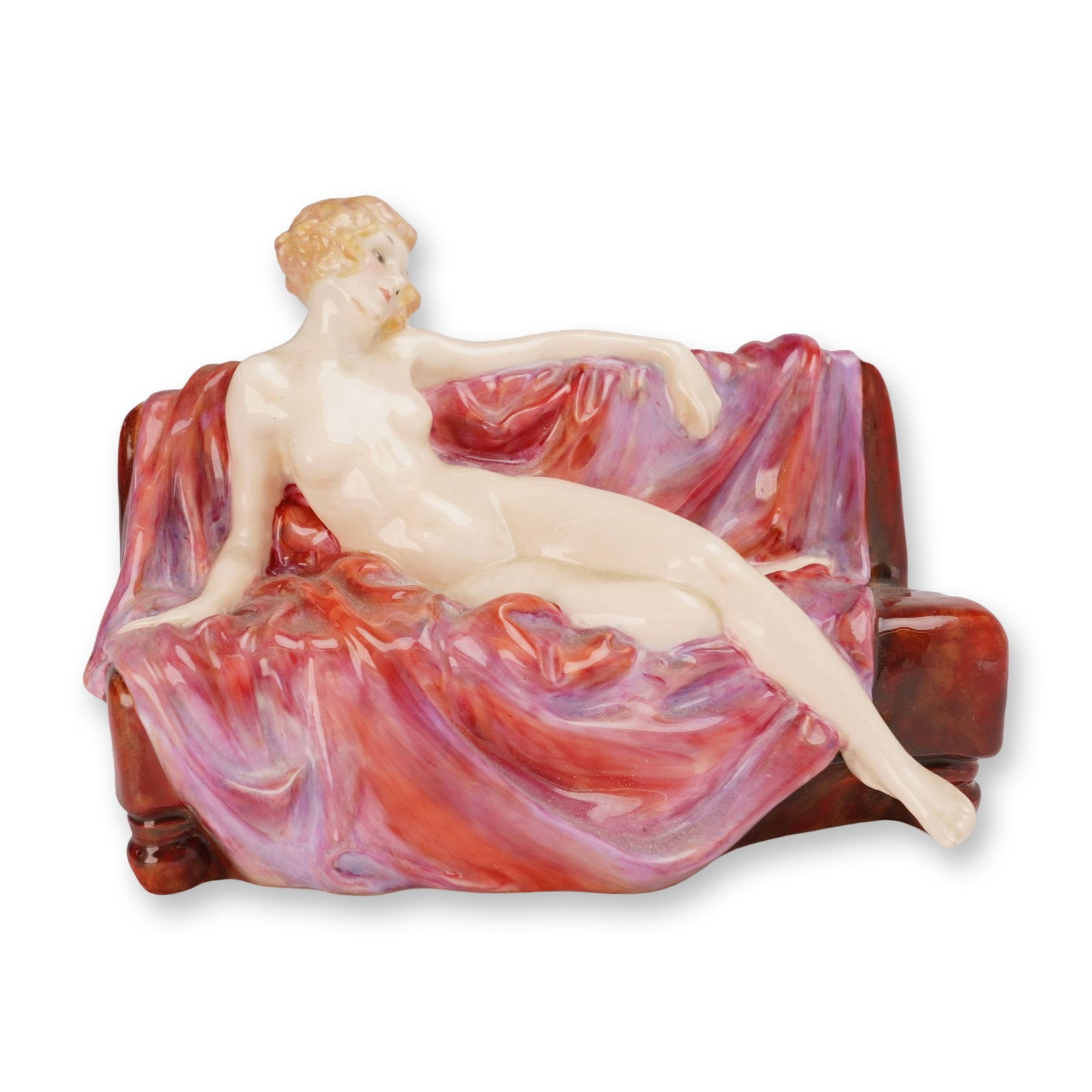 Royal Doulton Porcelain Figurine, Siesta HN1305: Designed by Leslie Harradine, circa 1929. The figurine depicts a reclining nude female figure resting on a sofa draped in a variegated pink, lavender, and red flowing cloth, set against a rich mottled