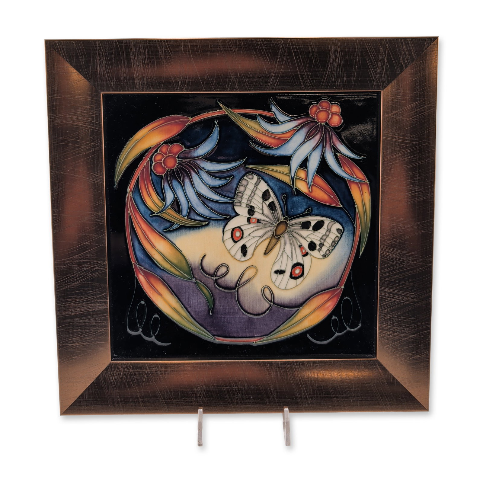 Framed Moorcroft Pottery by Sian Leeper Ceramic Title, Apollo: The design features a central butterfly motif surrounded by stylized flowers and foliage in shades of blue, orange, yellow, and cream on a dark ground. Housed in bronze-colored wooden frame. The rever