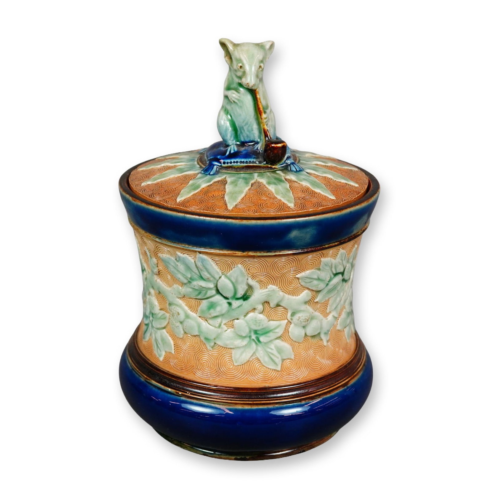 Doulton Lambeth by George Tinworth Stoneware Lidded Tobacco Jar: Textured ground with applied floral decoration in relief. Lid finial modeled as a seated mouse on a cushion holding a pipe. Tan and blue coloration with green accents. Doulton backstamp. Artist: Georg
