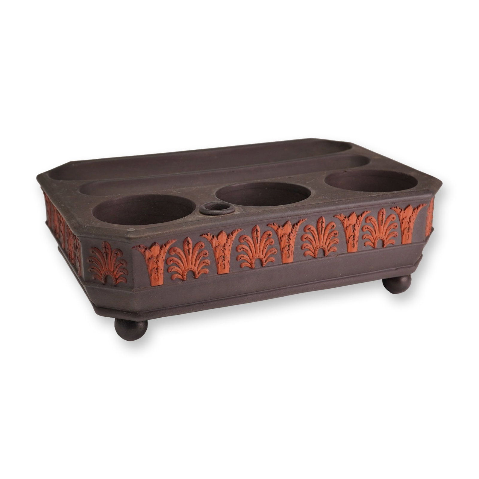Wedgwood Black Basalt and Rosso Antico Inkstand: A Wedgwood black basalt inkstand featuring applied rosso antico sprigged decoration. The rectangular form with canted corners is elevated on four ball feet. The top surface incorporates three large ci