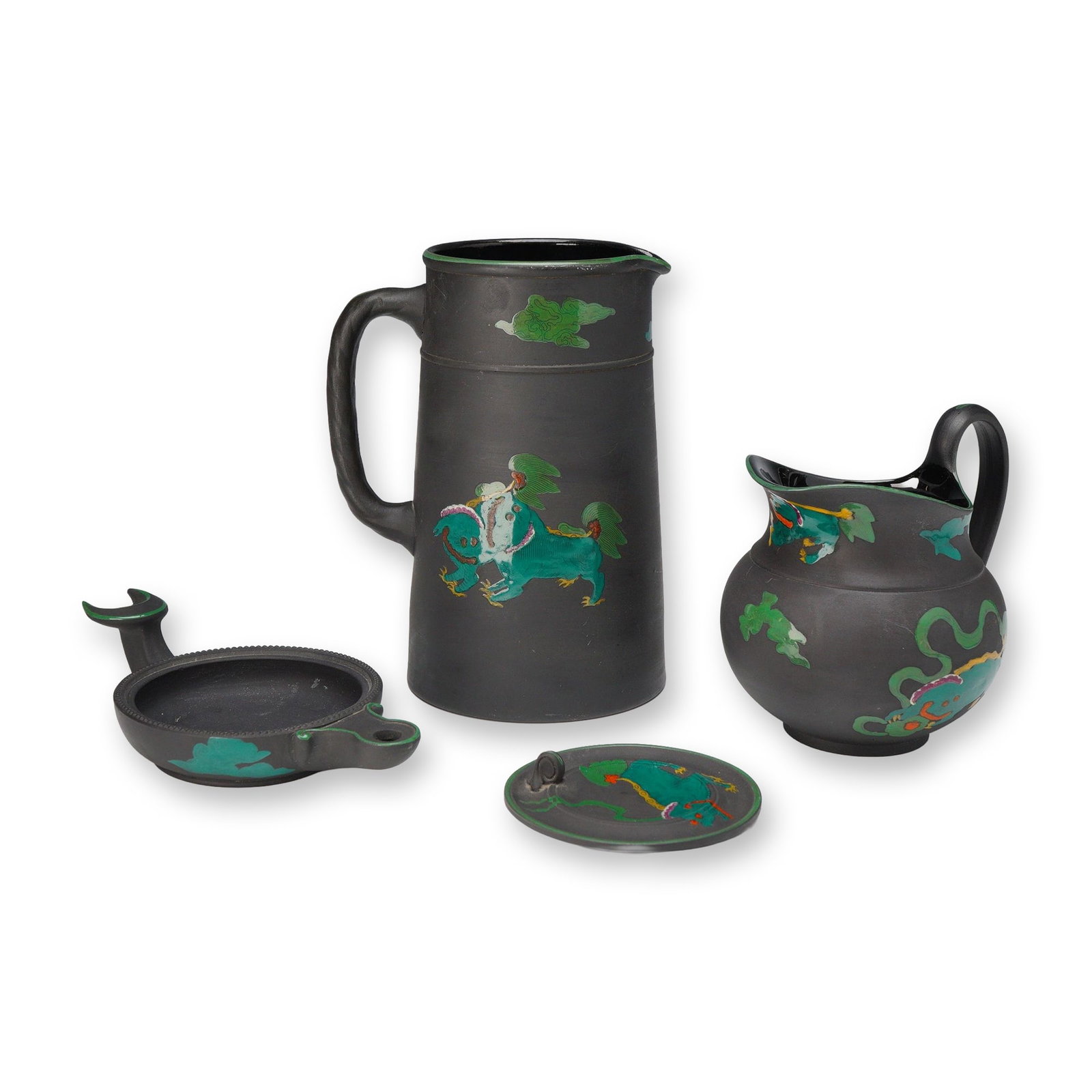 Three-Piece Wedgwood Black Basalt Dragon Kenlock Ware Pitcher, Creamer, and Oil Lamp: This three-piece collection of Wedgwood black basalt stoneware is decorated in the Dragon Kenlock Ware pattern. The set comprises a tall cylindrical pitcher with a simple loop handle, a globular cream