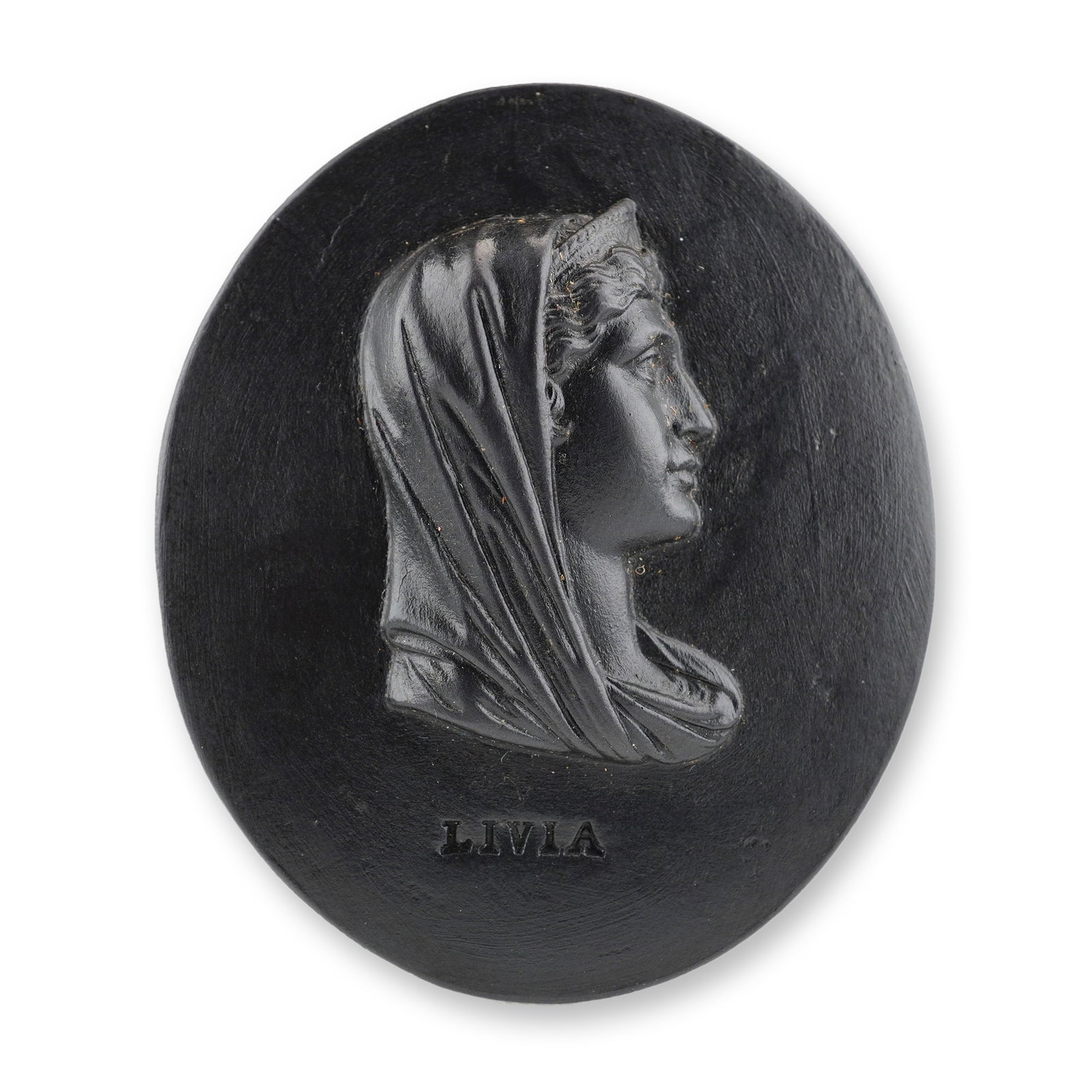 Wedgwood & Bentley Black Basalt Portrait Medallion of Livia: This oval relief-molded plaque is crafted from black basalt, a fine-grained black stoneware. The medallion features a profile portrait of the Roman Empress Livia Drusilla facing right. She is depicted