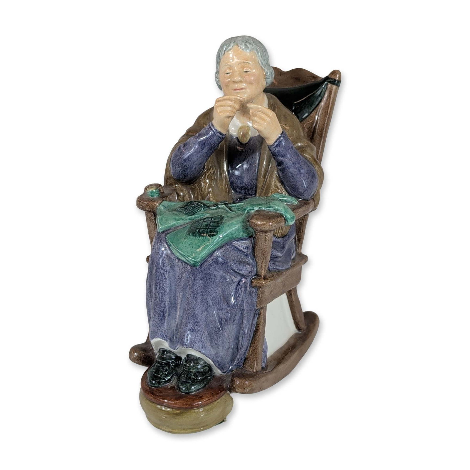 Royal Doulton A Stitch In Time Porcelain Figurine HN2352: Royal Doulton ceramic figurine titled A Stitch in Time, model HN2352. The glazed fine bone china piece depicts an elderly woman seated in a brown rocking chair, focused on her needlework. The figure i