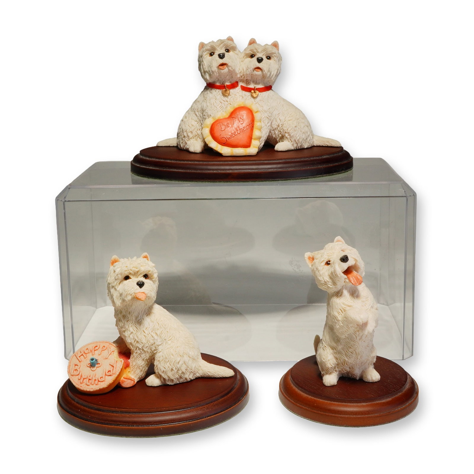 Three Sherratt & Simpson West Highland White Terrier Figurines with Bases: These hand-painted pieces feature realistic textural detailing of the breed's white coat. The group includes a pair of dogs adorned with red collars and a heart inscribed Be My Sweetheart, a single