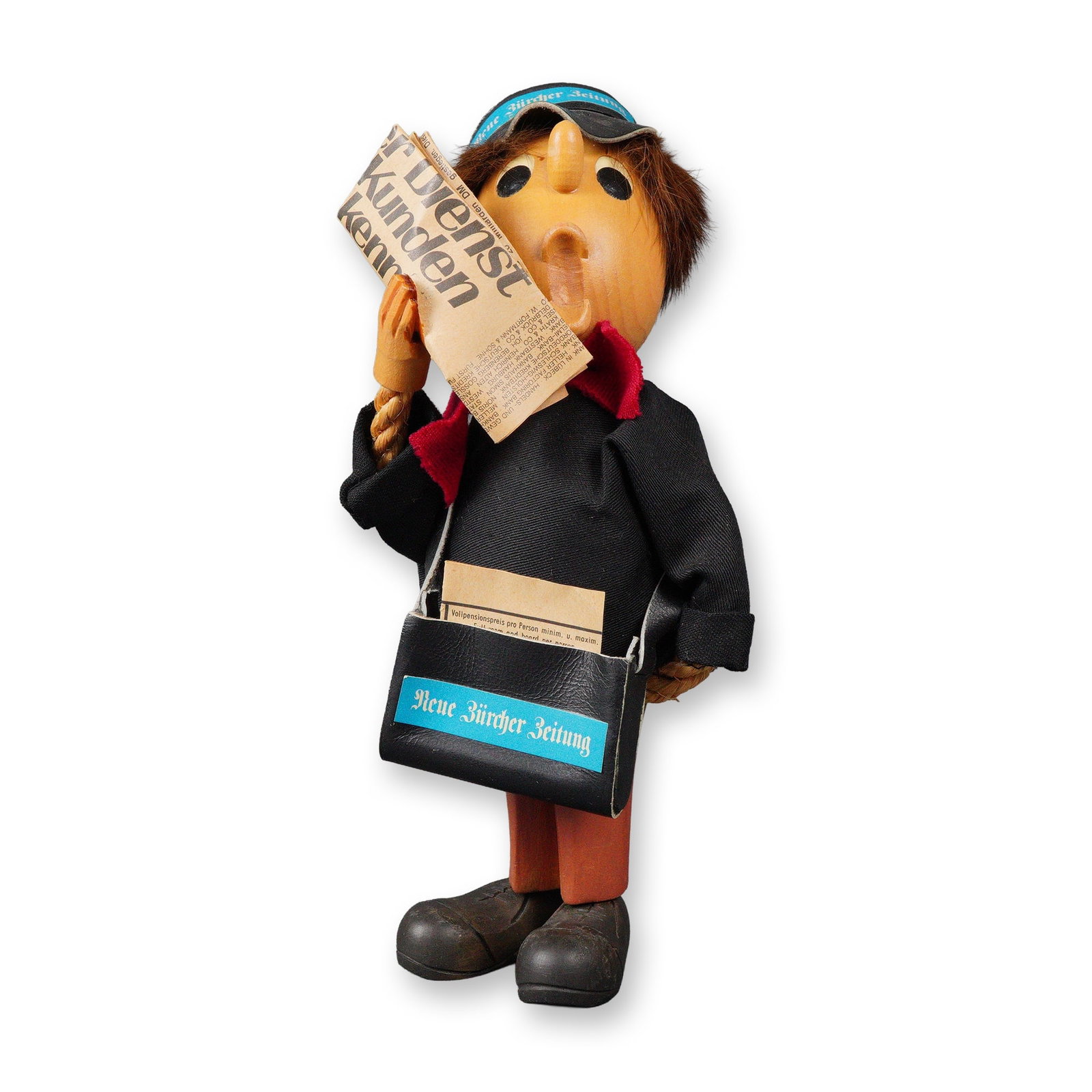 Anri Romer Casy Boys Carved Wood Newsboy Figurine: The figure features a carved wooden head with exaggerated features, hands, legs, and shoes. It is dressed in fabric clothing in black and orange, a red fabric scarf, and a black cap and shoulder bag,