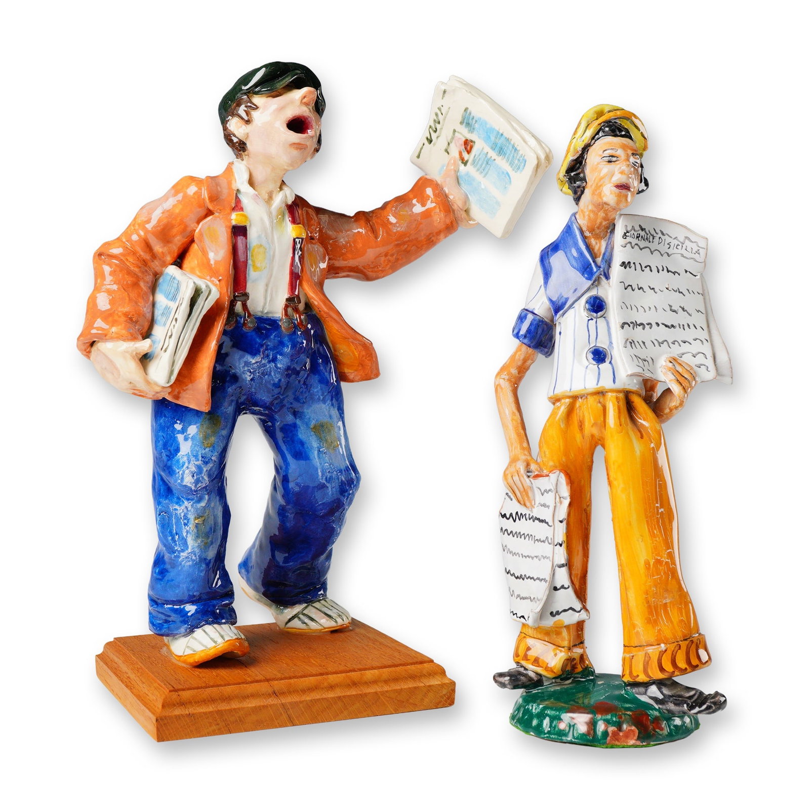 A Pair of Ceramic Newsboy Figurines: A grouping of 2pc figurines crafted from brightly glazed and polychrome painted ceramic, executed in an expressive, stylized manner, depicting newsboys holding papers. The larger figure is mounted on