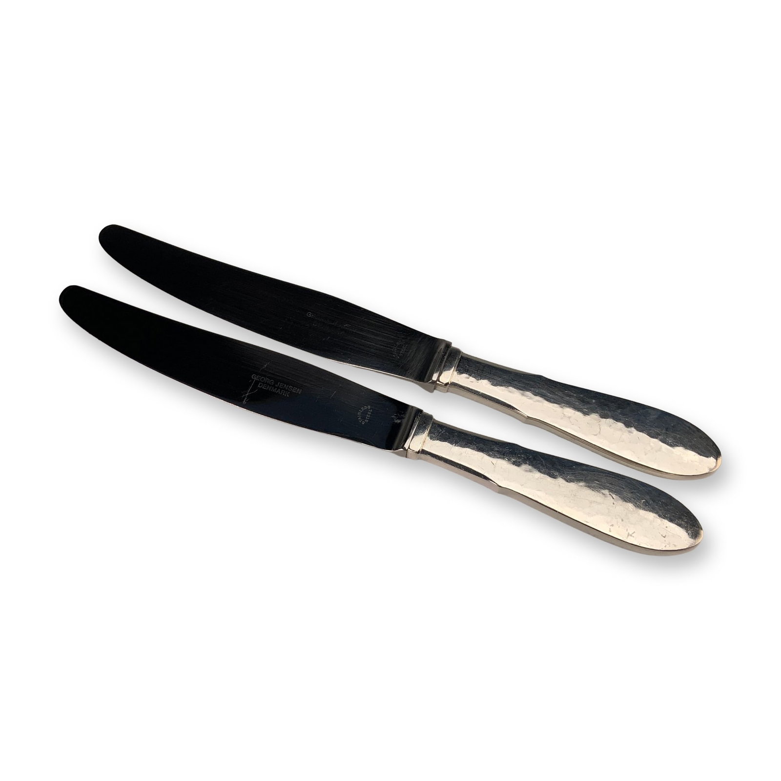 A Pair of Georg Jensen Denmark Mermaid Pattern EPNS Knives: A pair of Georg Jensen silverplate knives in the Mermaid pattern. These pieces feature the characteristic hand-hammered finish and flared handles associated with this Danish design. The handles are co