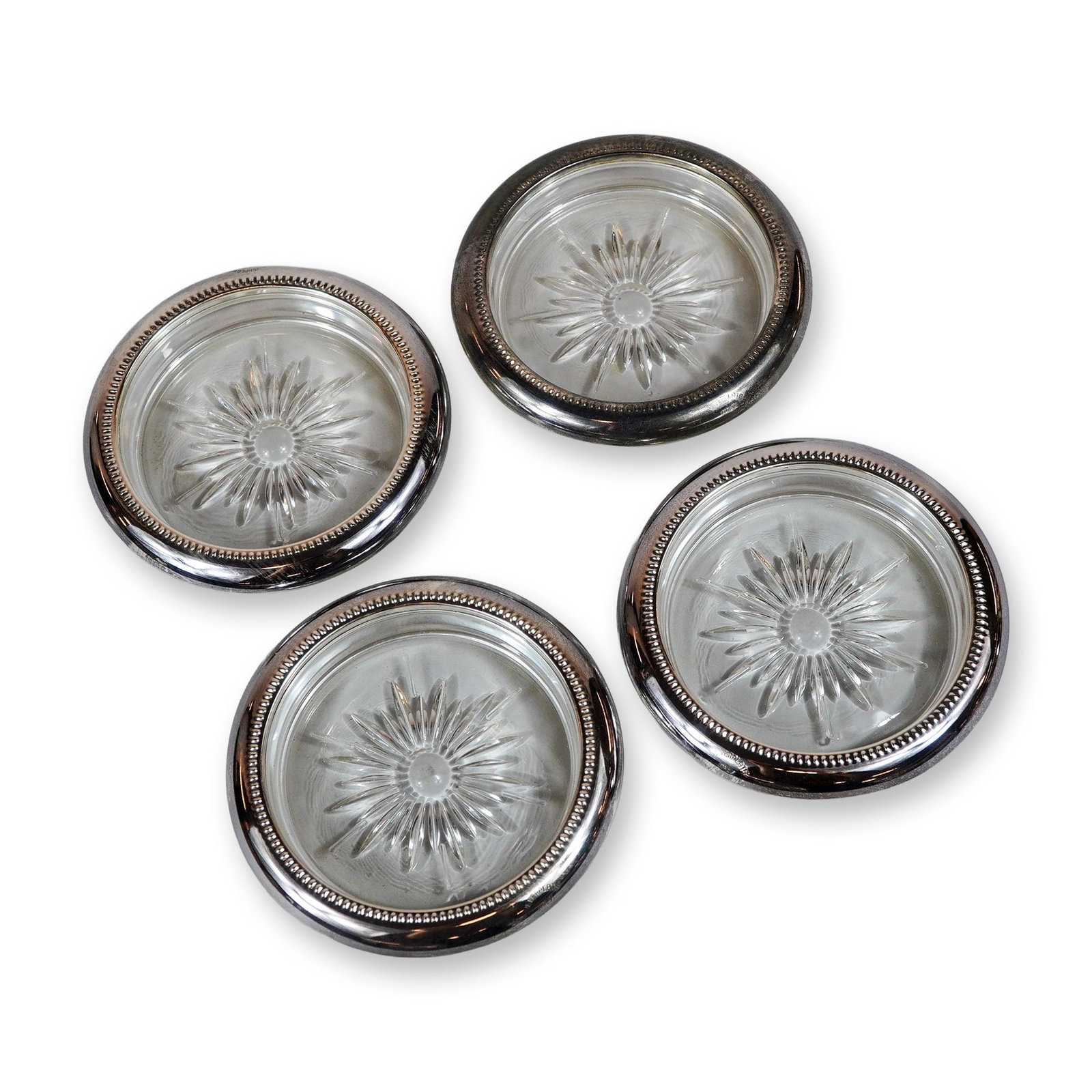 4pc Leonard Italy Style Glass Coasters: Leonard Italy style. Set of four beverage coasters in silver tone and glass, featuring molded starburst patterns to the inserts. The circular silver-plated rims are finished with a decorative beaded b