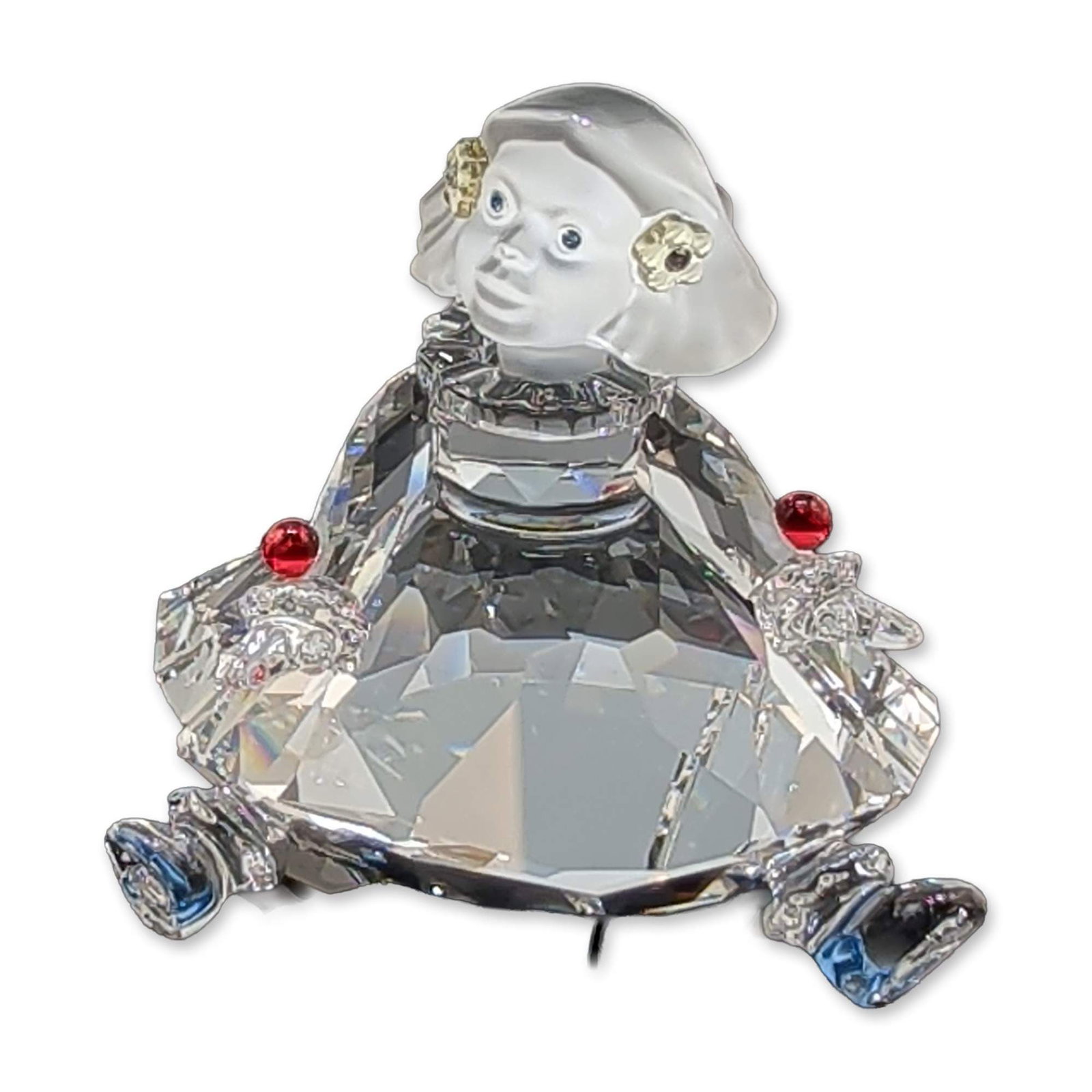 Swarovski Crystal Cheerful Times Doll Figurine: Swarovski seated doll figurine from the Cheerful Times collection constructed in faceted clear crystal with a frosted crystal head and flower. Decorative features include painted blue eyes, yellow cry