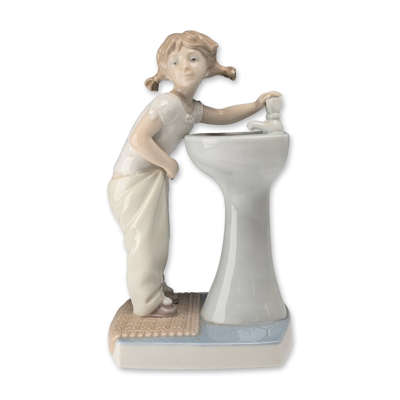 Lladro Spanish Porcelain Figurine Clean Up Time: Lladro (Spain, late 20th century). Clean Up Time (model #4838) glazed porcelain figurine, featuring a young girl with blonde pigtails standing at a sink. The figure is dressed in a white short-sleeved