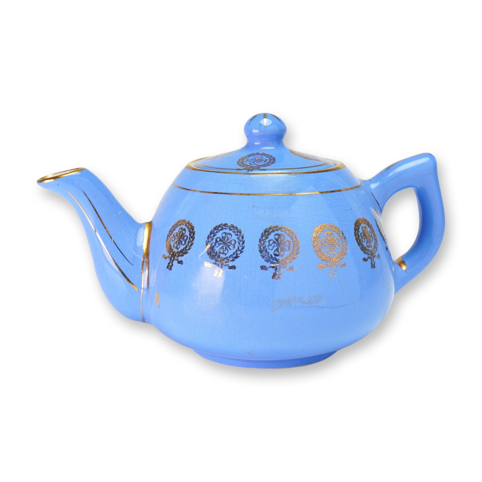 Weller Pottery Periwinkle Blue and Gilded Wreath Teapot with Lid: The vessel features a vibrant periwinkle blue gloss glaze decorated with a repeating horizontal band of gilded laurel wreath medallions, each centering a quatrefoil motif. The design is further