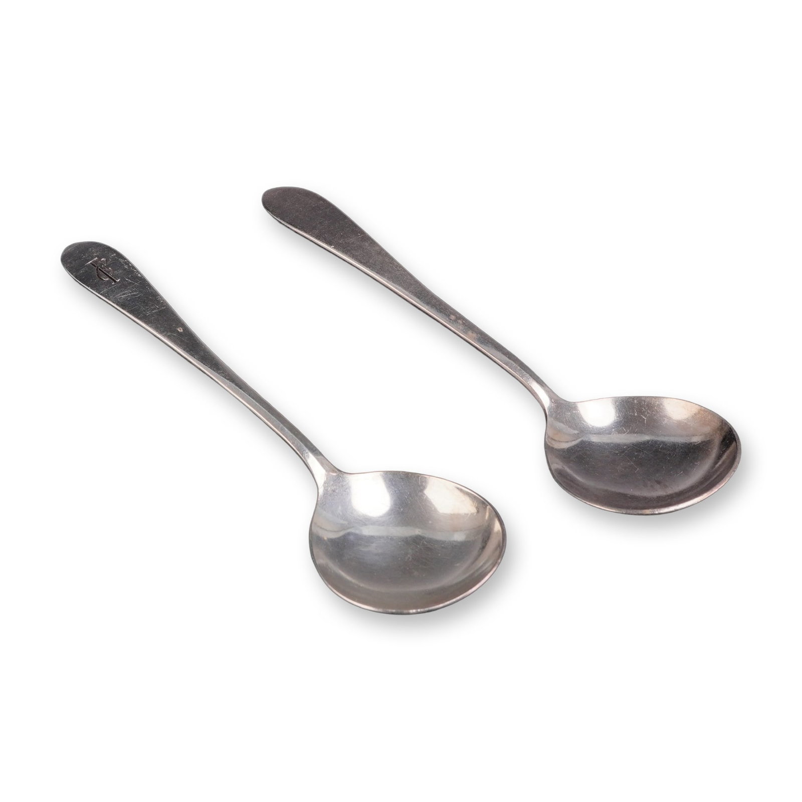 A Pair of International Silver Co. Silver-Plated Spoons: A pair of silverplated round-bowl soup spoons manufactured by the International Silver Company. The spoons feature a circular bowl and a flat, unadorned handle with a rounded terminal. The terminal of