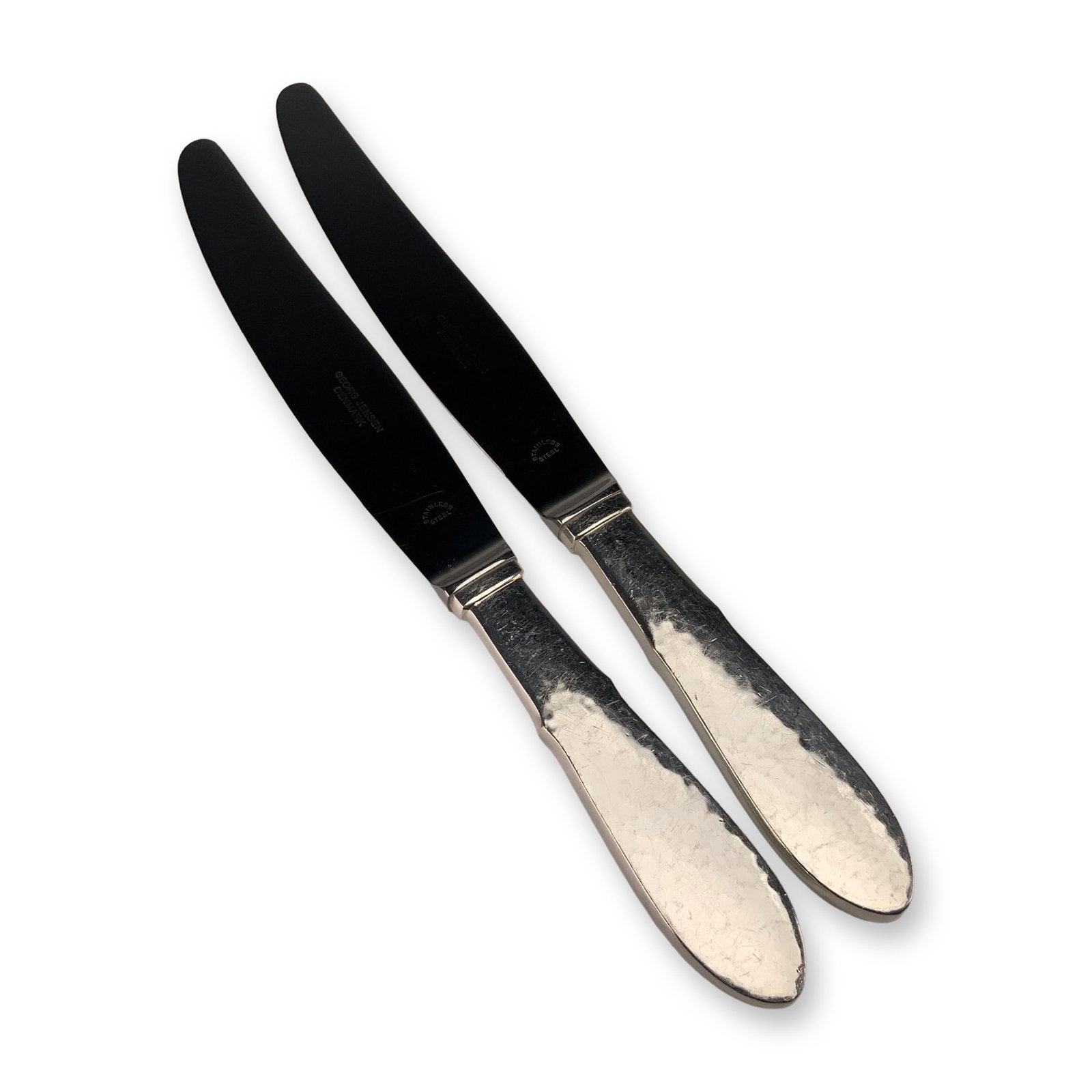 A Pair of Georg Jensen Denmark Mermaid Pattern EPNS Knives: This pair of dinner knives is in the Mermaid pattern by Georg Jensen, Denmark. The handles are constructed of silver-plated nickel silver, marked EPNS, and feature a hammered texture with faceted